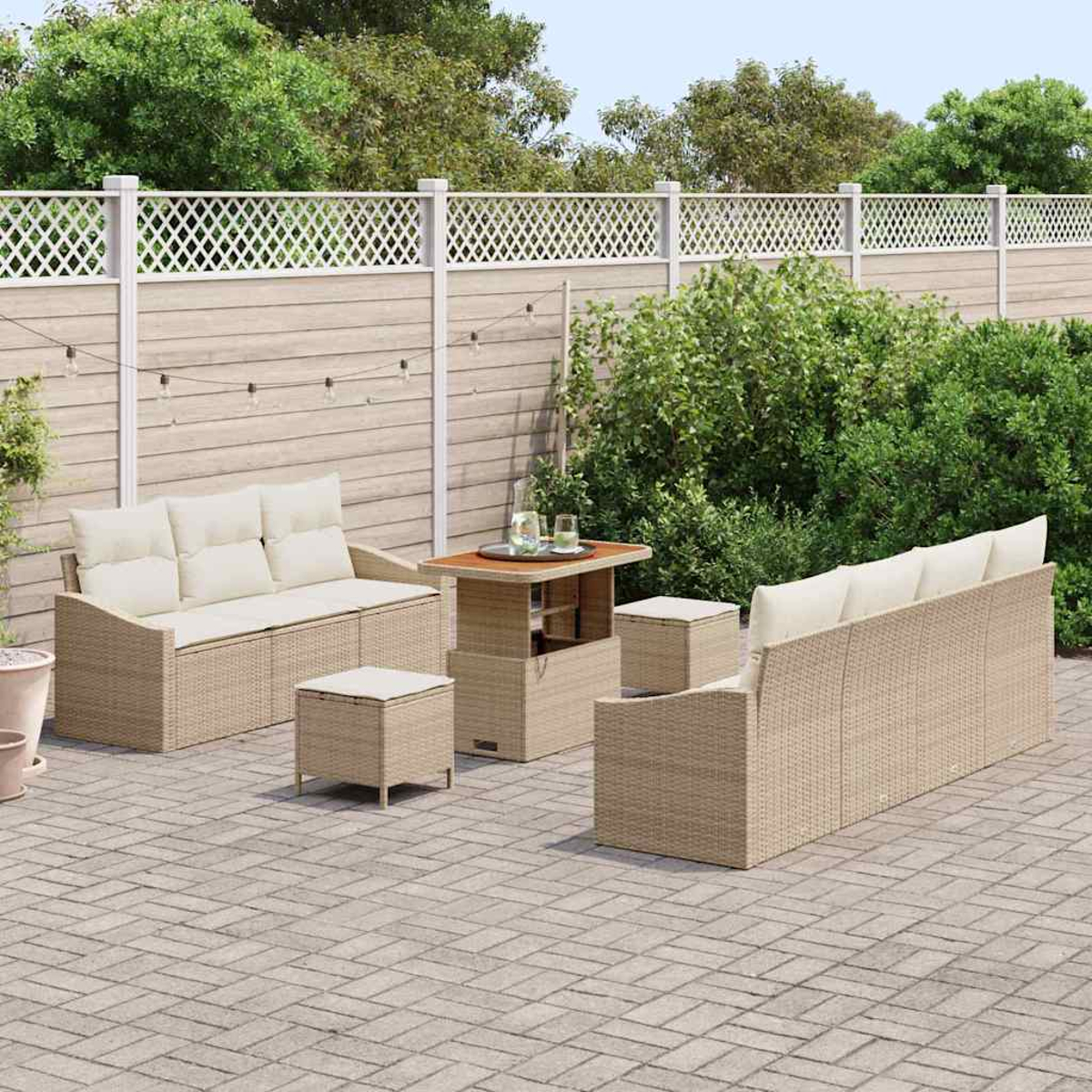 Garten-Terrassenset mit beigen Sofas, einem Tisch und Ottomanen. Vor einem Holzzaun und Grün. Gepflasterte Terrasse.