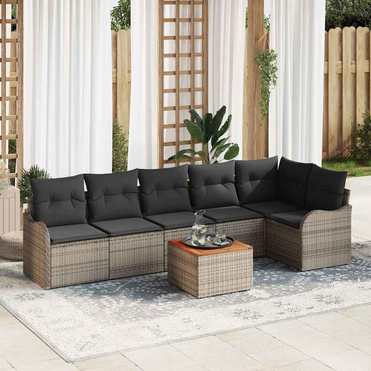 Outdoor-Ecksofa mit dunklen Kissen. Davor steht ein kleiner Tisch mit Getränken. Weiße Vorhänge und Pflanzen sind im Hintergrund.
