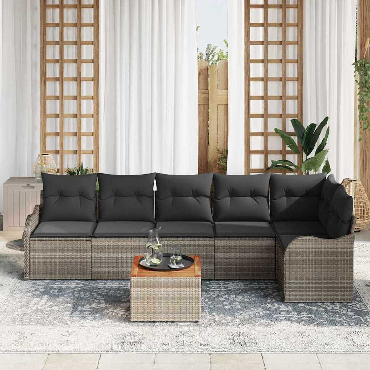 Outdoor-Ecksofa mit grauen Kissen und einem kleinen Tisch, auf einem gemusterten Teppich, mit weißen Vorhängen und Holzgitter.