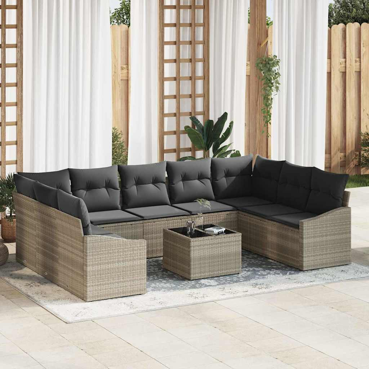 Outdoor-Ecksofa mit grauen Kissen und einem kleinen Tisch. Weiße Vorhänge und Holzzaun im Hintergrund. Pflanzen sind sichtbar.