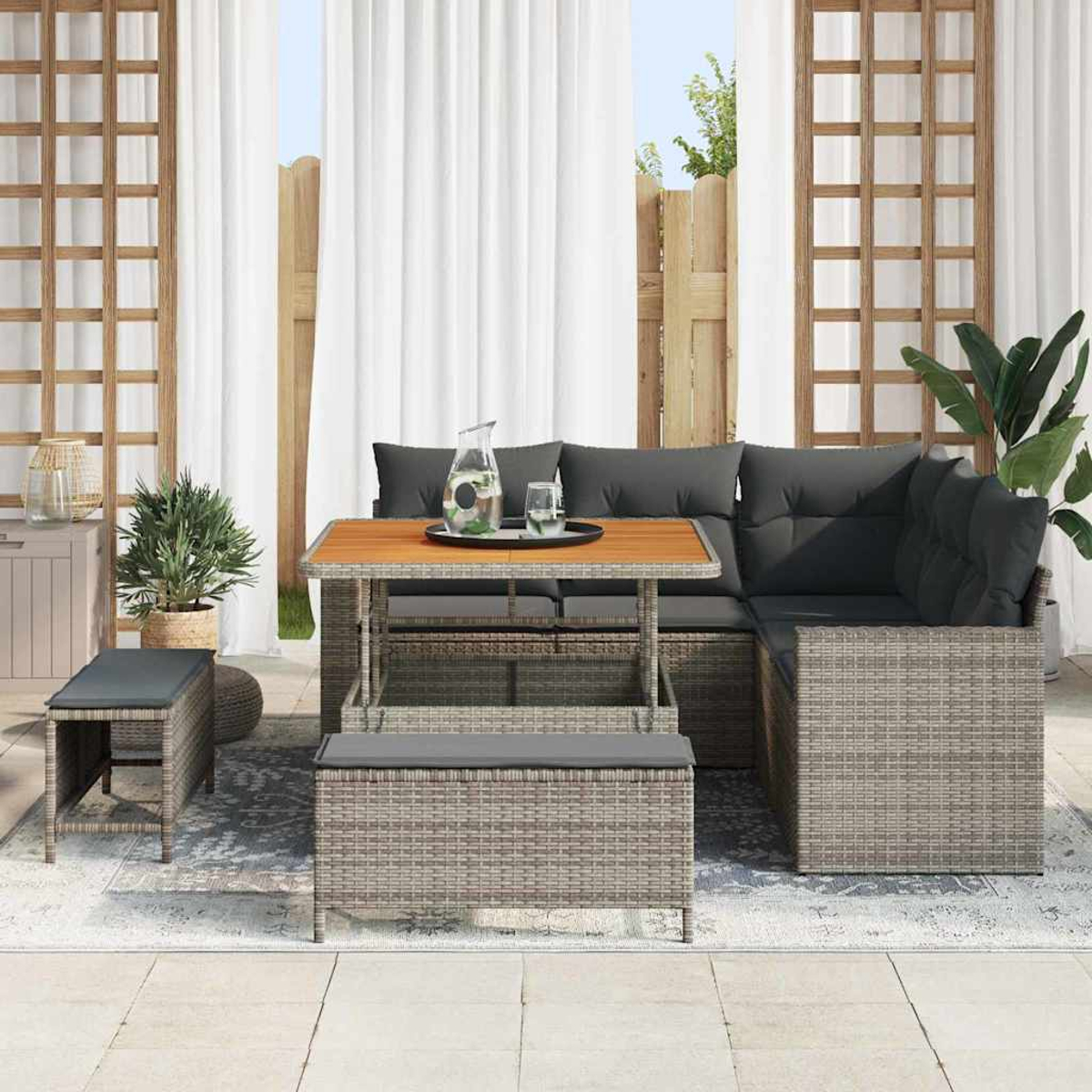 Garten-Terrassenset mit Sofa, Tisch und Bank. Graue Kissen auf gewebten Möbeln. Eine Kanne und Gläser stehen auf dem Tisch.