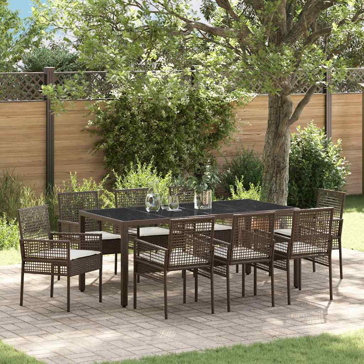 Juego de comedor al aire libre con mesa oscura, sillas y cojines en un patio pavimentado, rodeado de vegetación y valla de madera.
