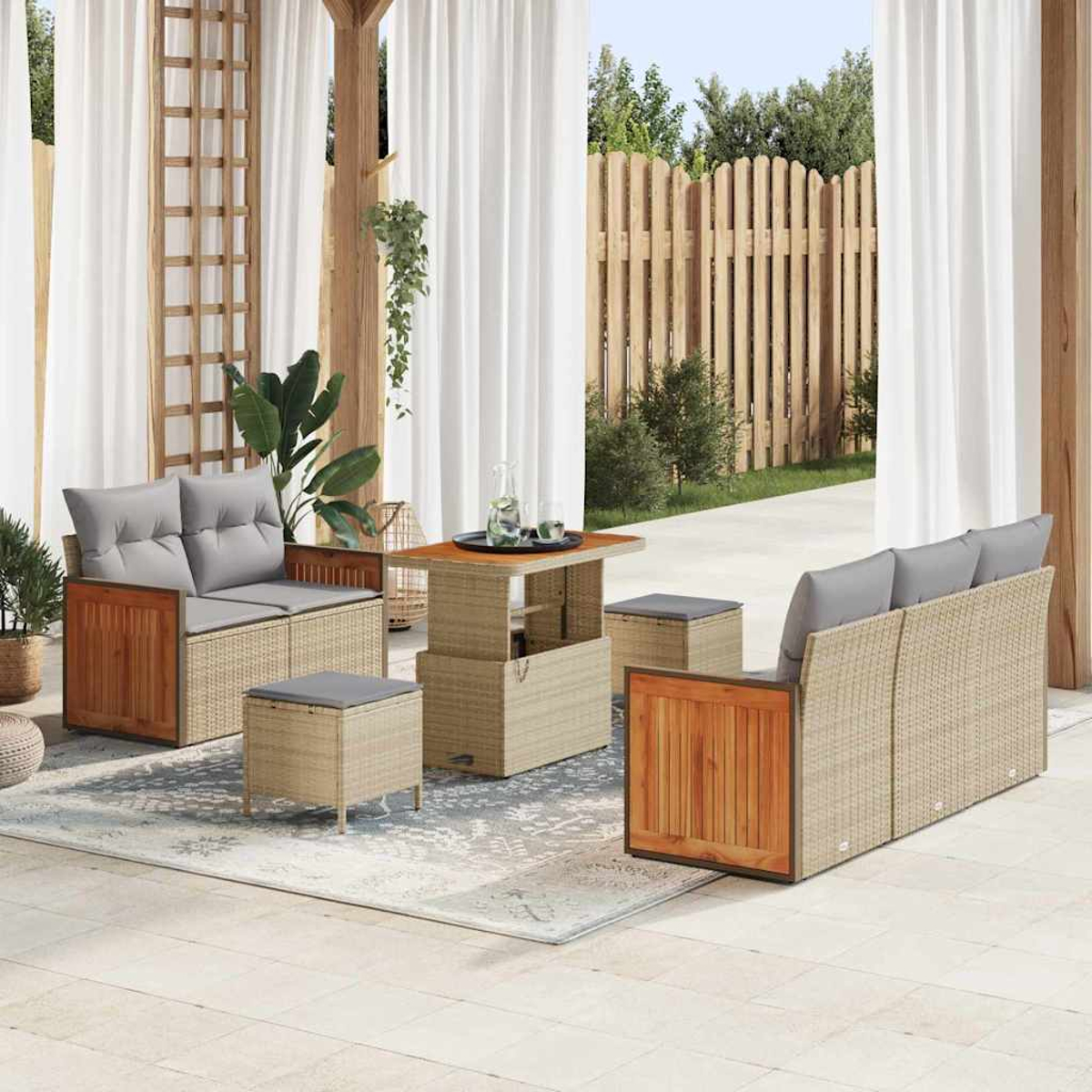 Set da patio esterno con divano, pouf e tavolo. Accenti in legno, cuscini grigi e tappeto neutro. Tende bianche e recinzione in legno sullo sfondo.