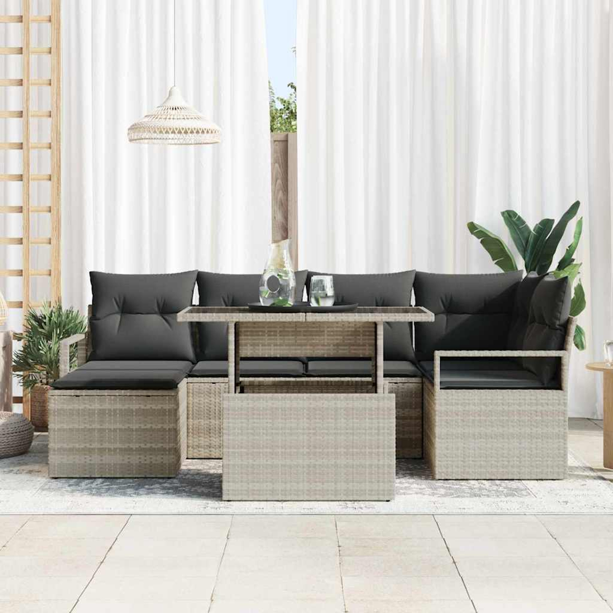 Outdoor-Wicker-Sofagarnitur mit grauen Kissen, Glastisch und weißen Vorhängen. Enthält Pflanzen und eine Hängeleuchte.