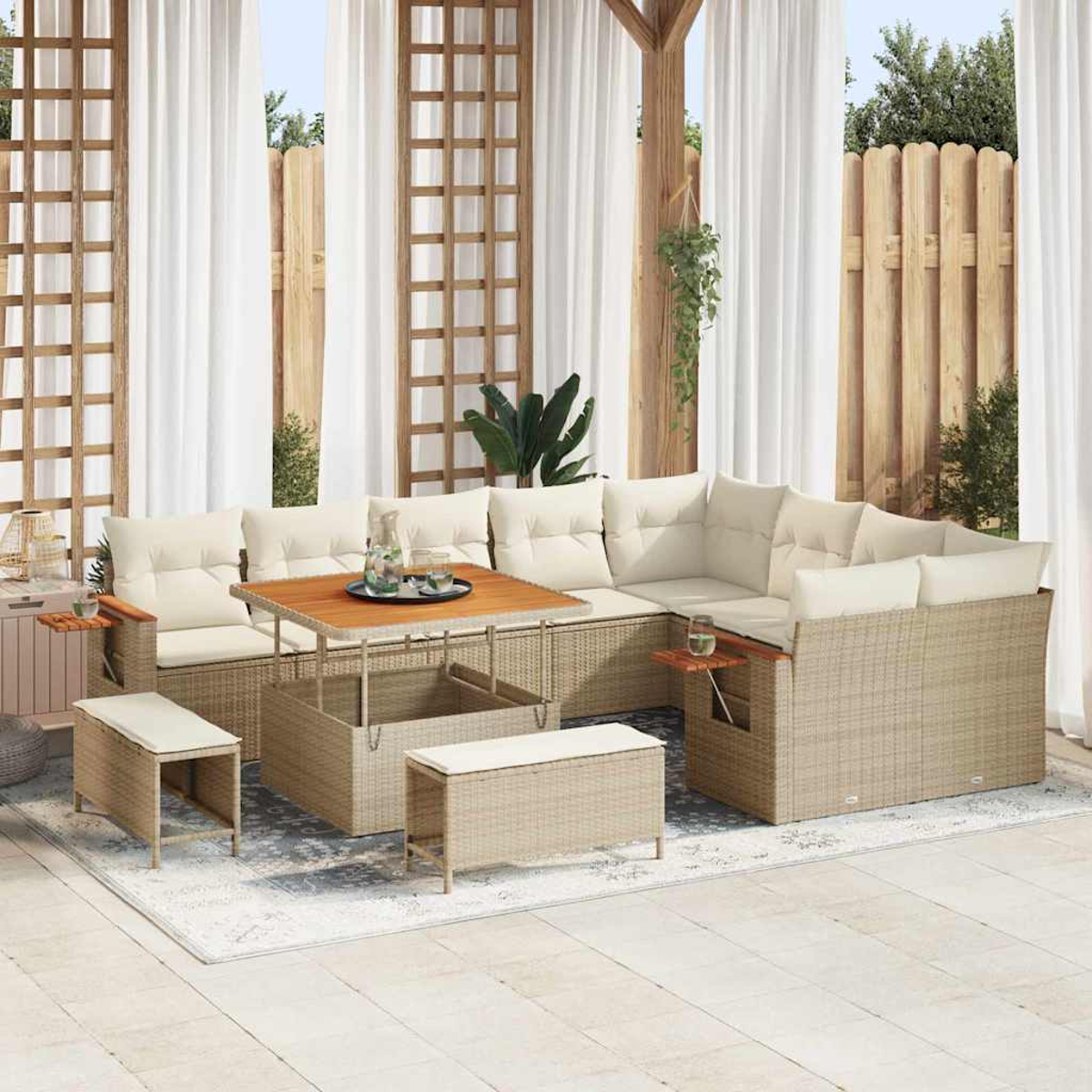 Gartenmöbel-Set aus Korbgeflecht mit cremefarbenen Kissen und einem Holztisch. Enthält ein Ecksofa, Bänke und einen Teppich, unter weißen Vorhängen.