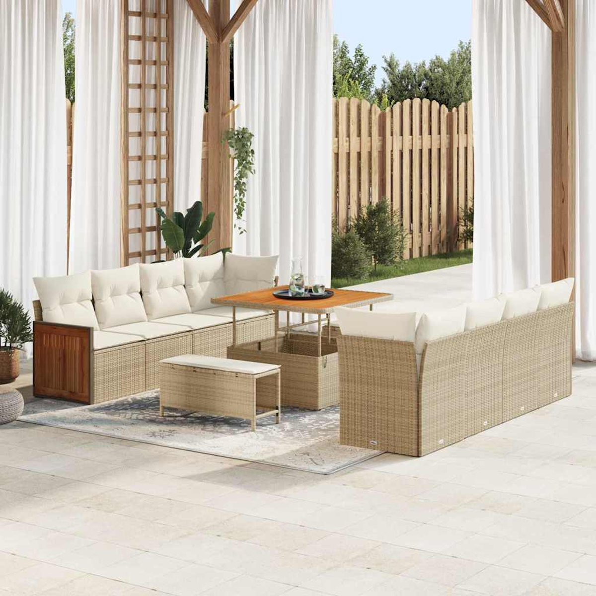 Außenbereich mit Rattansitzmöbeln, Holztisch und weißen Vorhängen. Im Hintergrund ein Holzzaun und Pflanzen.