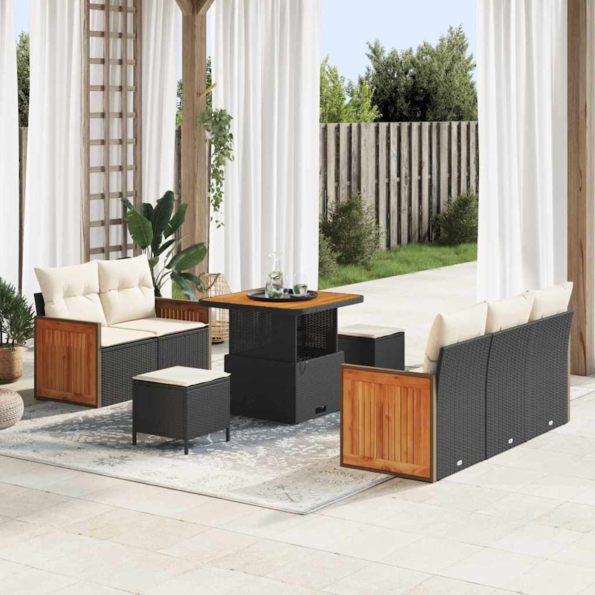 Set di mobili da patio. Include tavolo, divani e pouf. Tende bianche e recinzione in legno sullo sfondo.