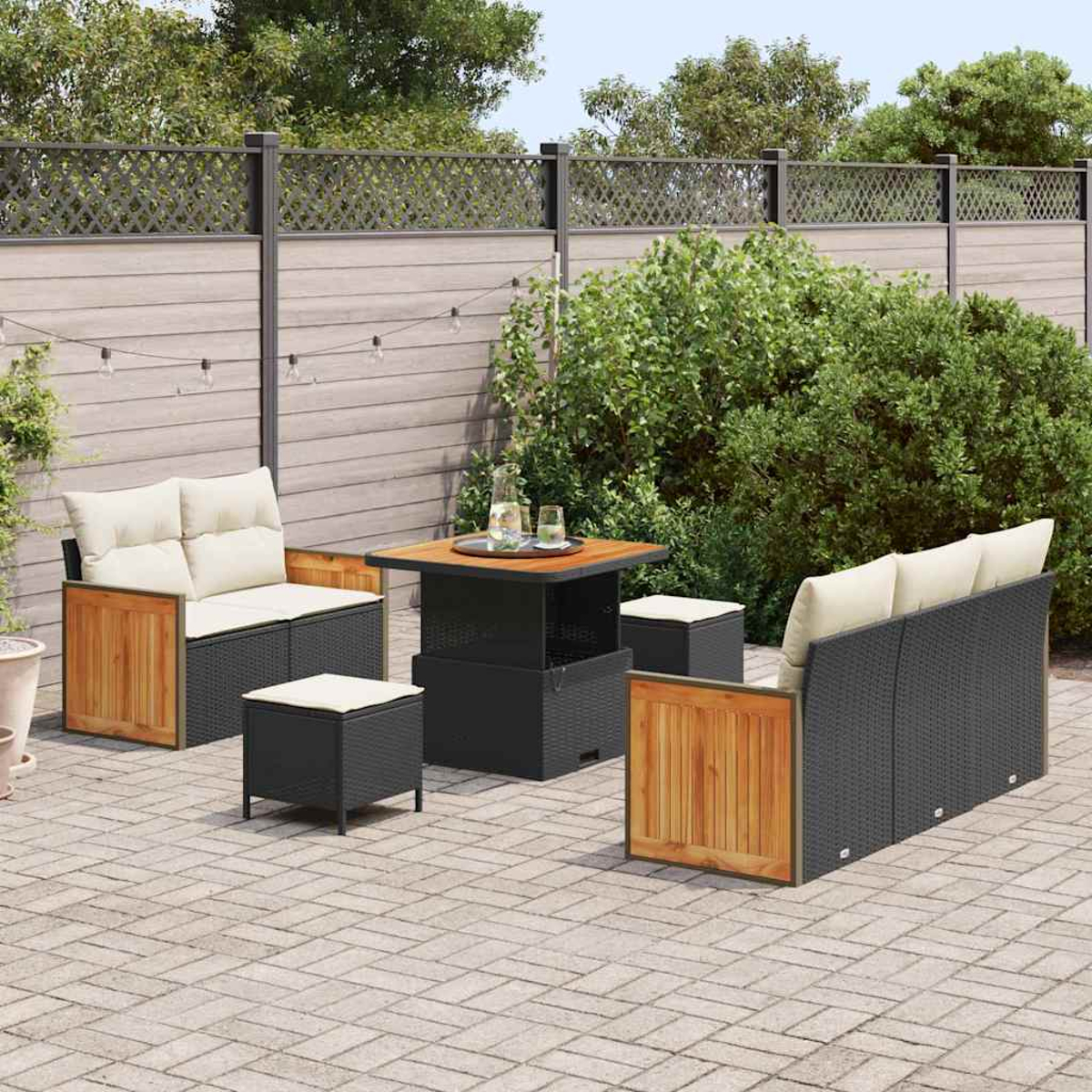 Set da patio con mobili in vimini neri, dettagli in legno e cuscini color crema. Un tavolo e degli sgabelli sono disposti su un patio in mattoni, verde sullo sfondo.