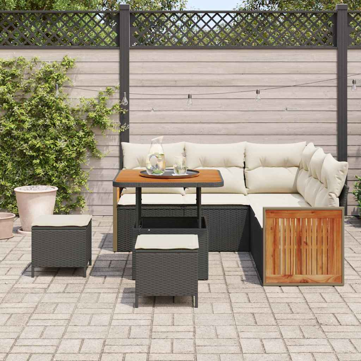 Gartenmöbel-Set mit beigefarbenen Kissen, einem Holztisch und zwei grauen Korbstühlen. Im Hintergrund ein Holzzaun.
