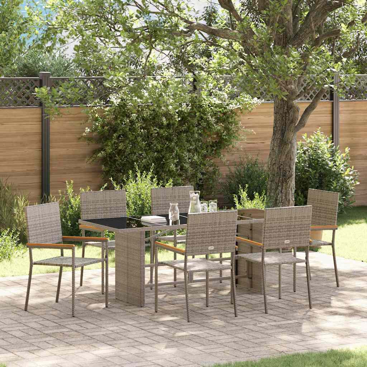 Ein Ess-Set im Freien mit Tisch und Stühlen auf einer Terrasse. Im Hintergrund ein Baum, mit Holzzaun und Grün.
