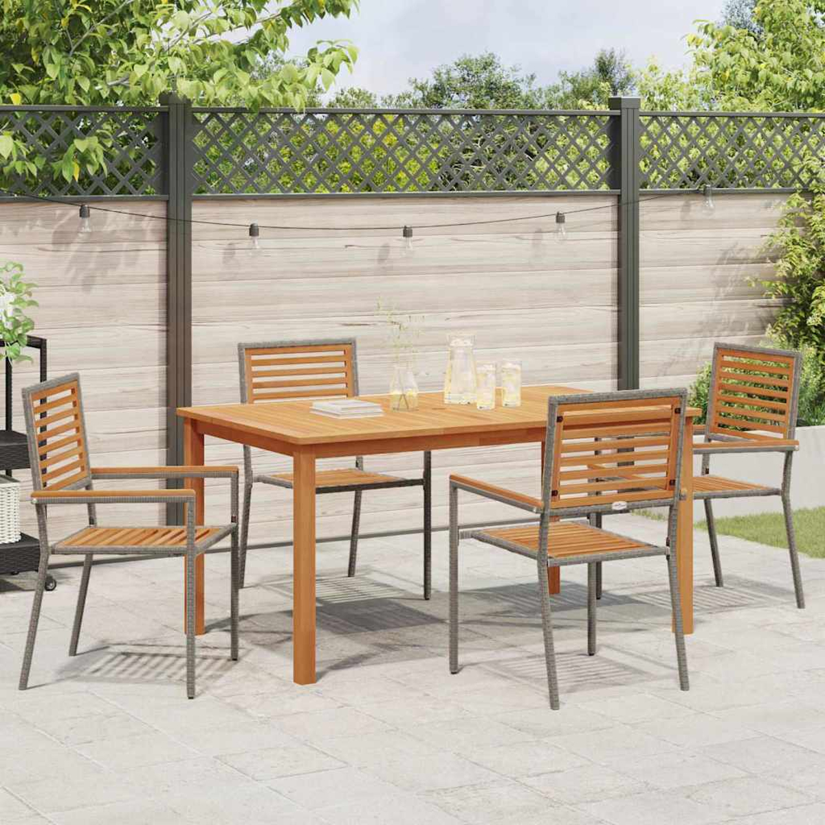 Ein Holztisch mit vier Stühlen steht auf einer Terrasse. Im Hintergrund ist ein Zaun mit Pflanzen und Lichterketten zu sehen.