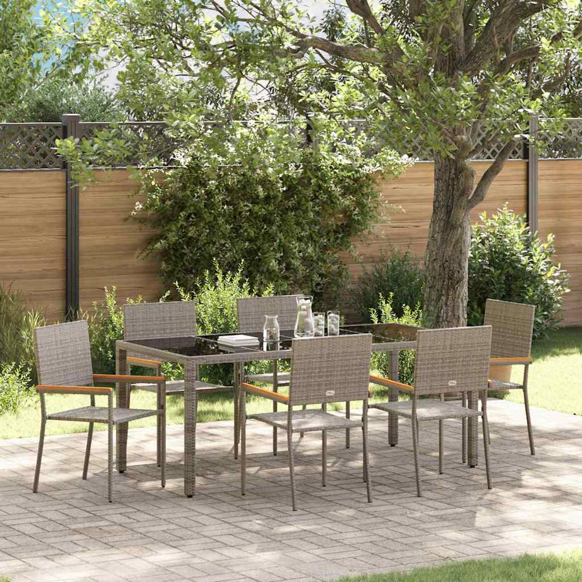 Essgruppe im Freien auf einer Terrasse. Beinhaltet einen Tisch mit sechs Stühlen, einen Krug und Gläser, umgeben von Bäumen und einem Holzzaun.