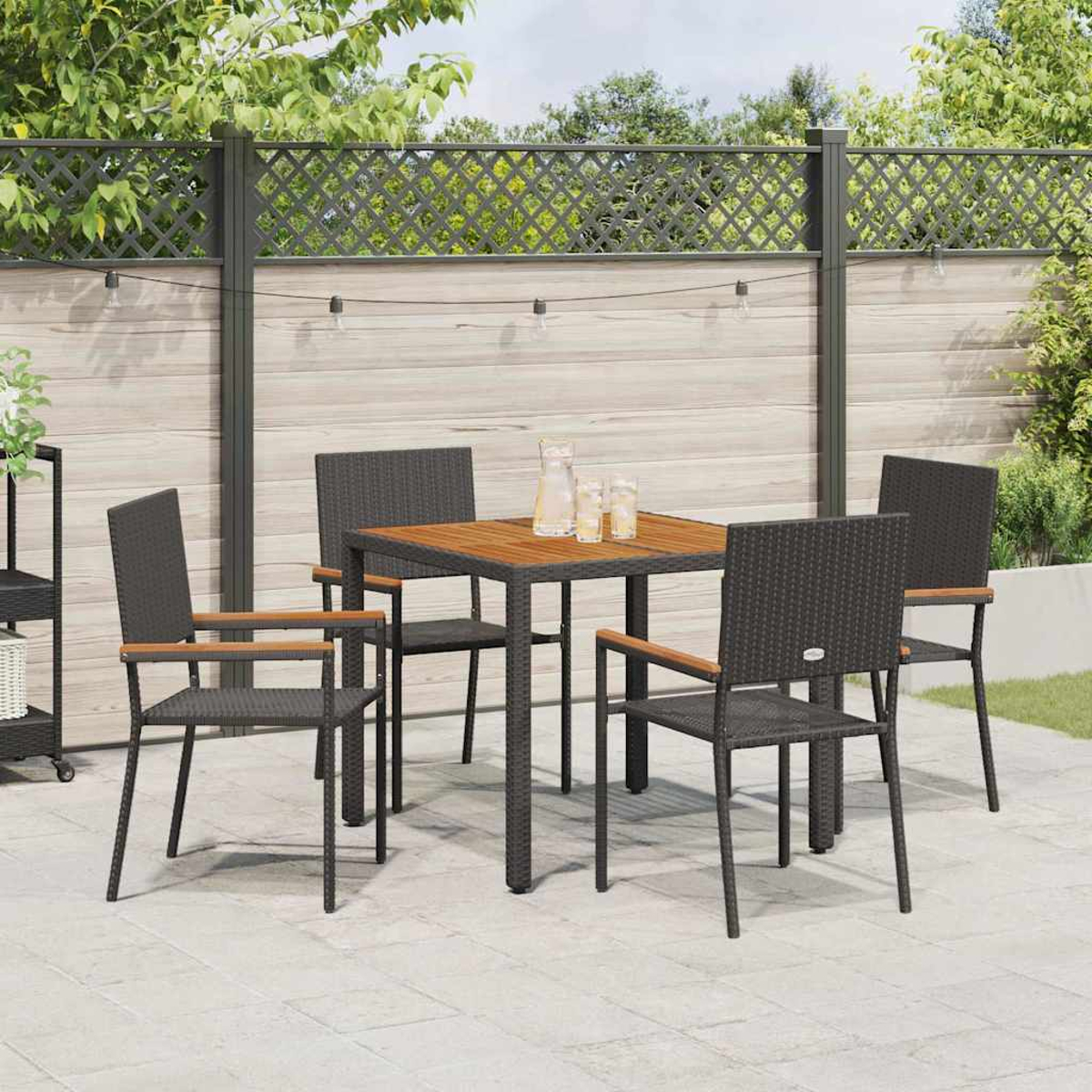 Terrassenset im Freien: Tisch, vier Stühle, Getränke, Lichterkette und Zaun. Die Szene spielt auf einer Terrasse mit Grün im Hintergrund.