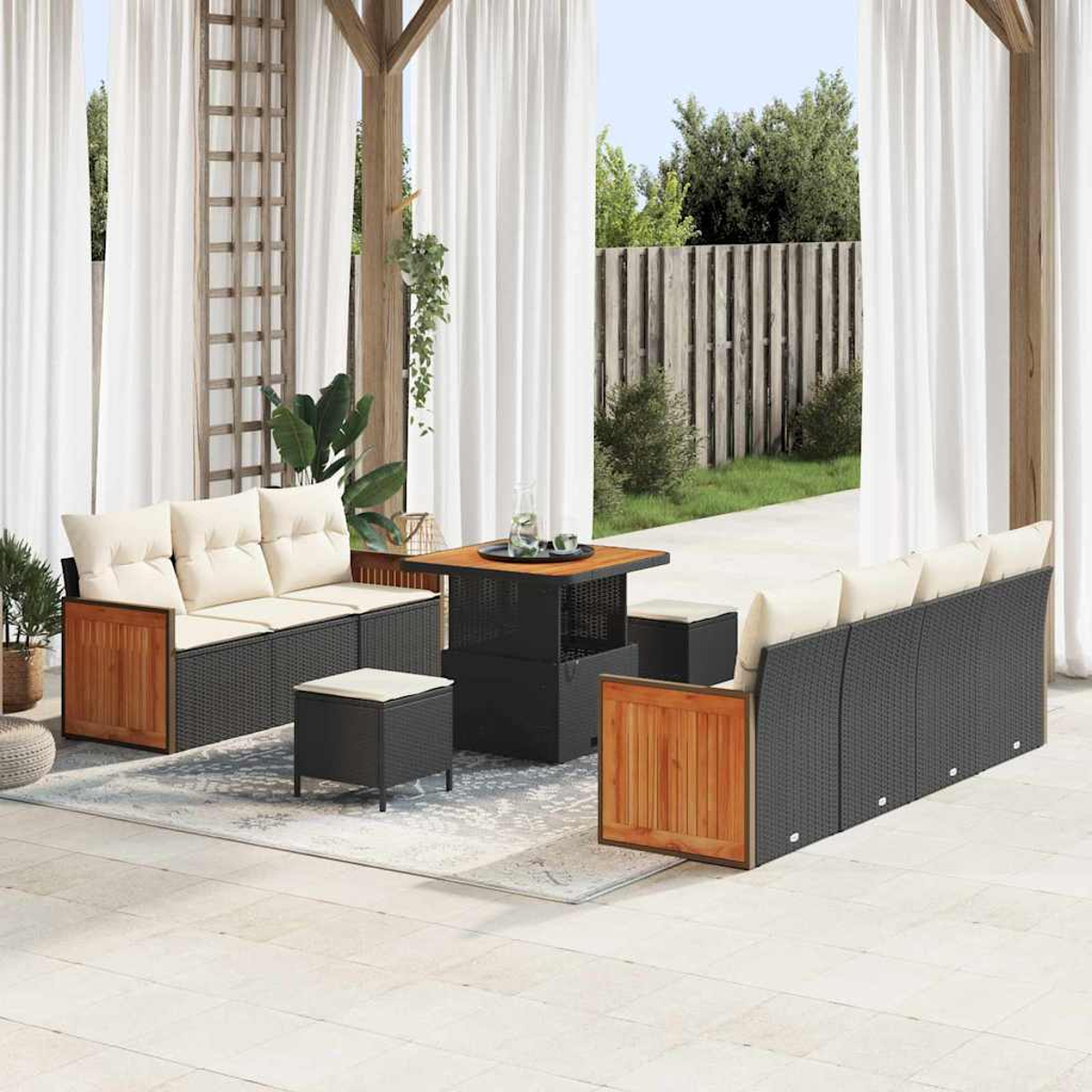 Set di mobili da esterno: divani in vimini, tavolo in legno, sgabelli, cuscini color crema. Tende bianche, pergola in legno e giardino verde.