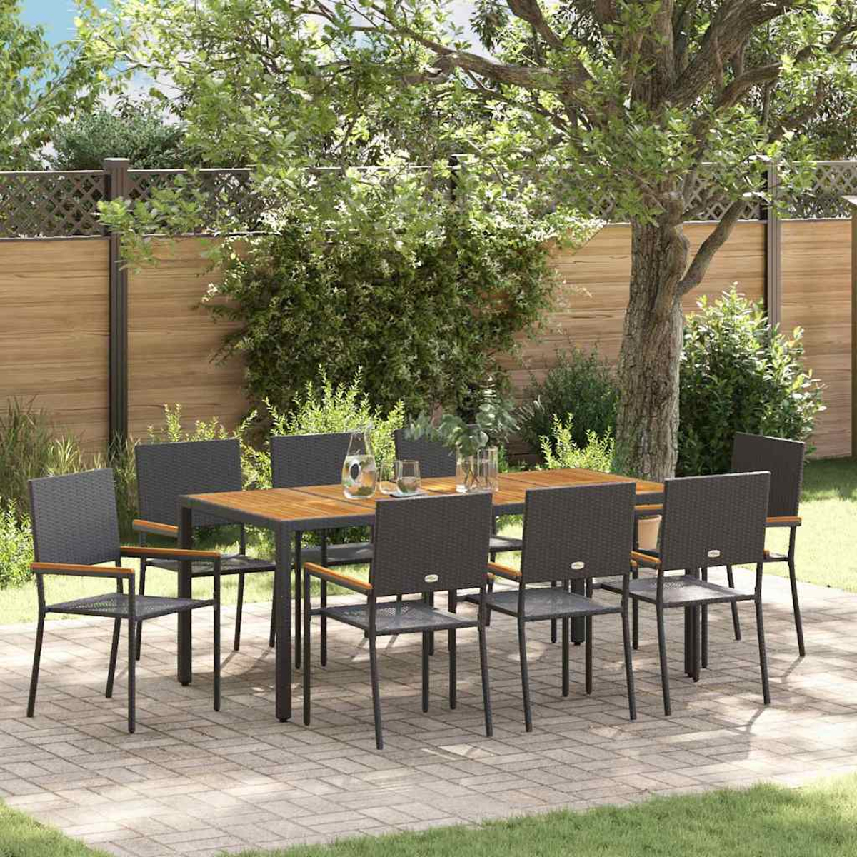 Essgruppe im Freien auf einer Terrasse. Ein Holztisch, umgeben von dunkelgrauen Stühlen. Der Hintergrund zeigt einen Holzzaun und grünes Laub.