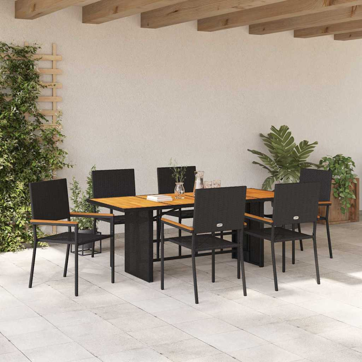 Juego de comedor al aire libre. Una mesa rectangular con sillas negras, sobre un patio embaldosado. Plantas verdes y una pared neutra al fondo.