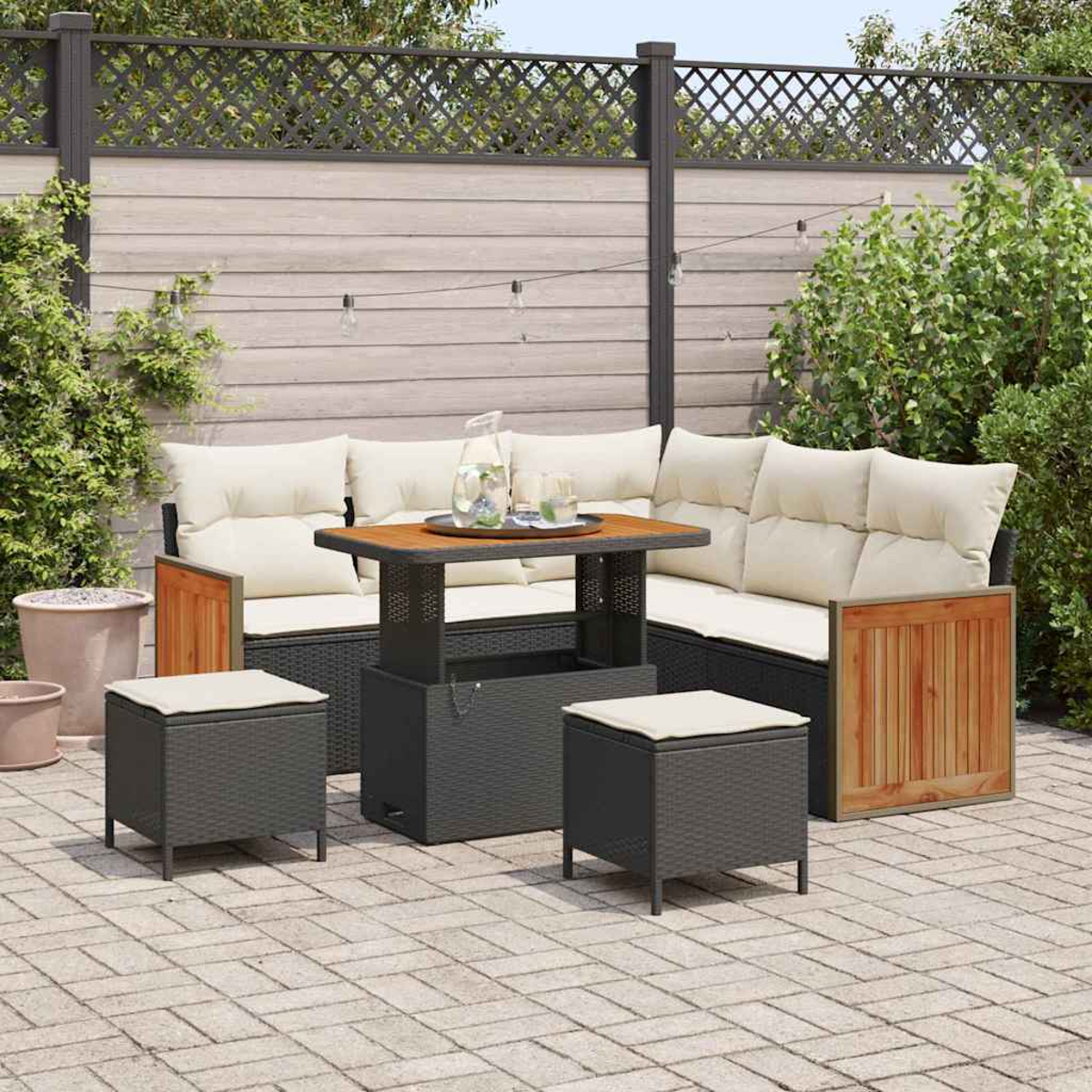 Juego de patio al aire libre con sofá, mesa y taburetes. Cojines beige, detalles de madera y bebidas en la mesa. Muebles de mimbre grises.