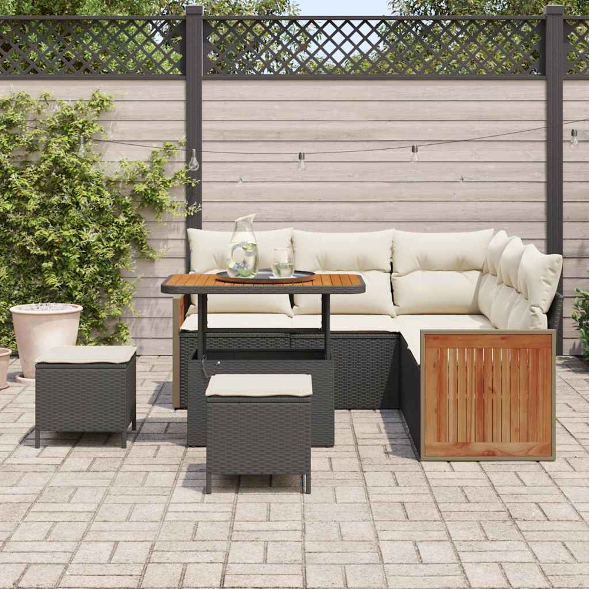 Juego de muebles de patio: sofá en forma de L con cojines crema, dos otomanas y una mesa pequeña. Valla de madera al fondo.