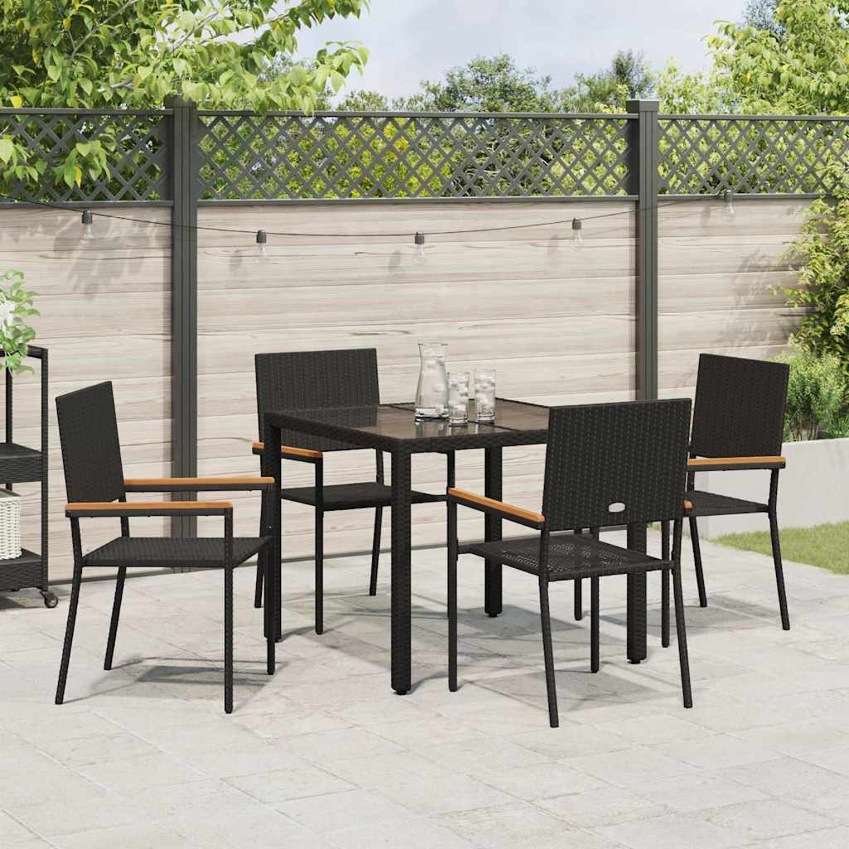 Terrassenset im Freien. Ein schwarzer Tisch und Stühle auf einer Steinterrasse. Holzzaun im Hintergrund mit Lichterketten.