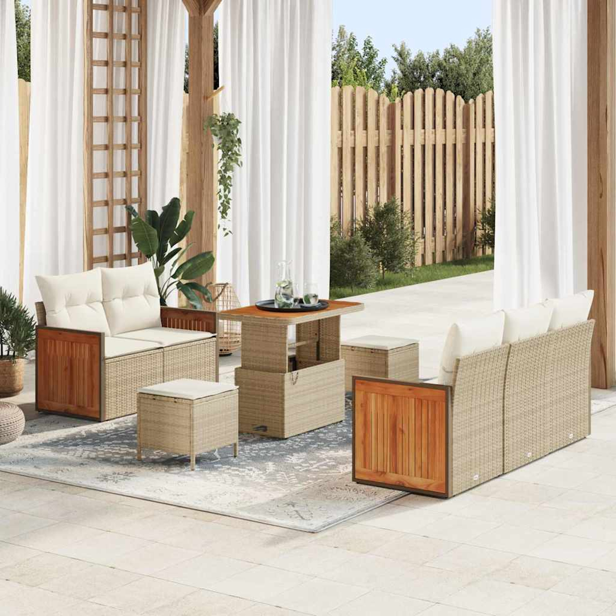 Set patio esterno con divano, due sedie, tavolo e pouf. Su un tappeto con tende bianche e recinzione in legno sullo sfondo.