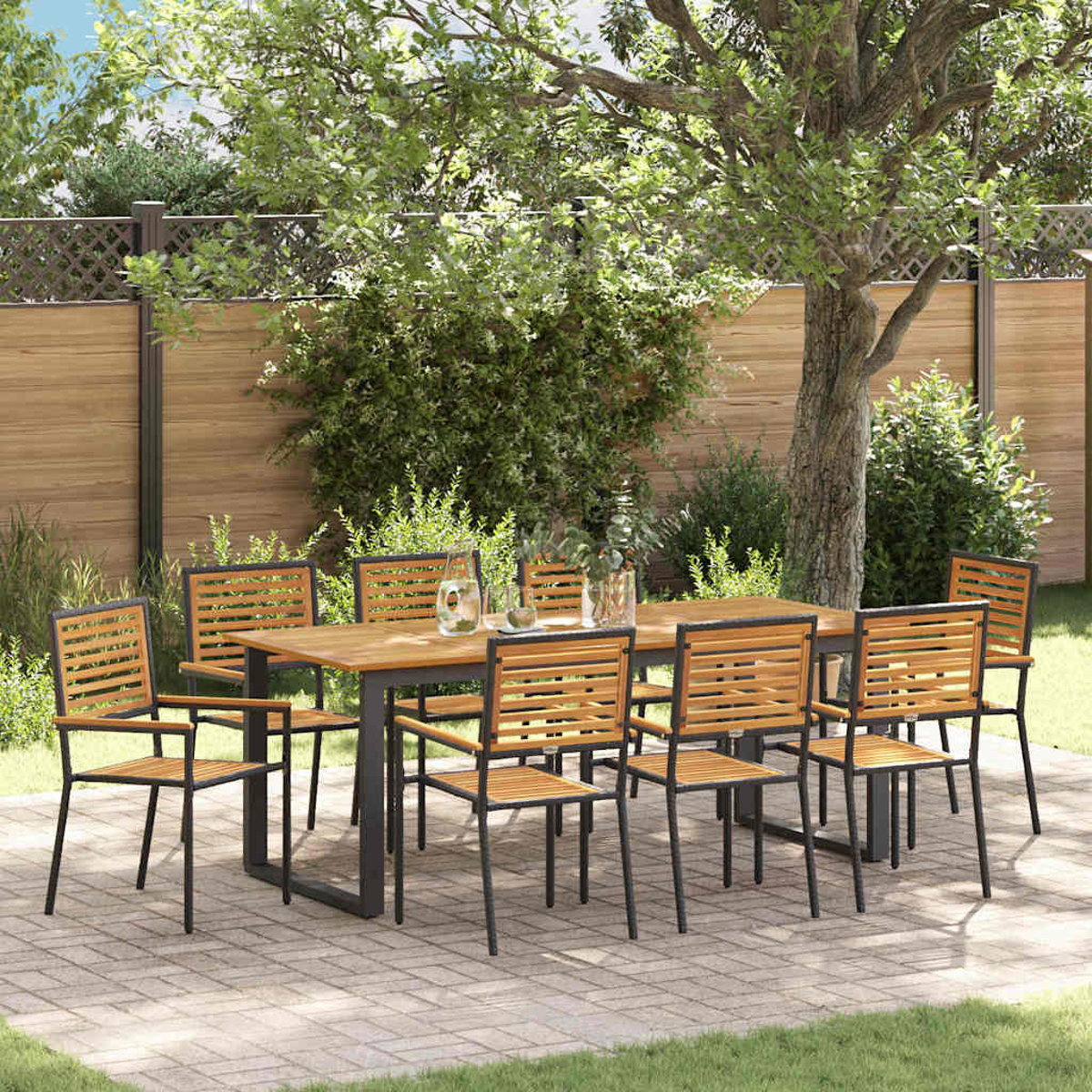 Set da pranzo all'aperto su un patio. Tavolo e sedie in legno, su pavimentazione in mattoni. Sfondo con recinzione in legno, alberi e vegetazione.