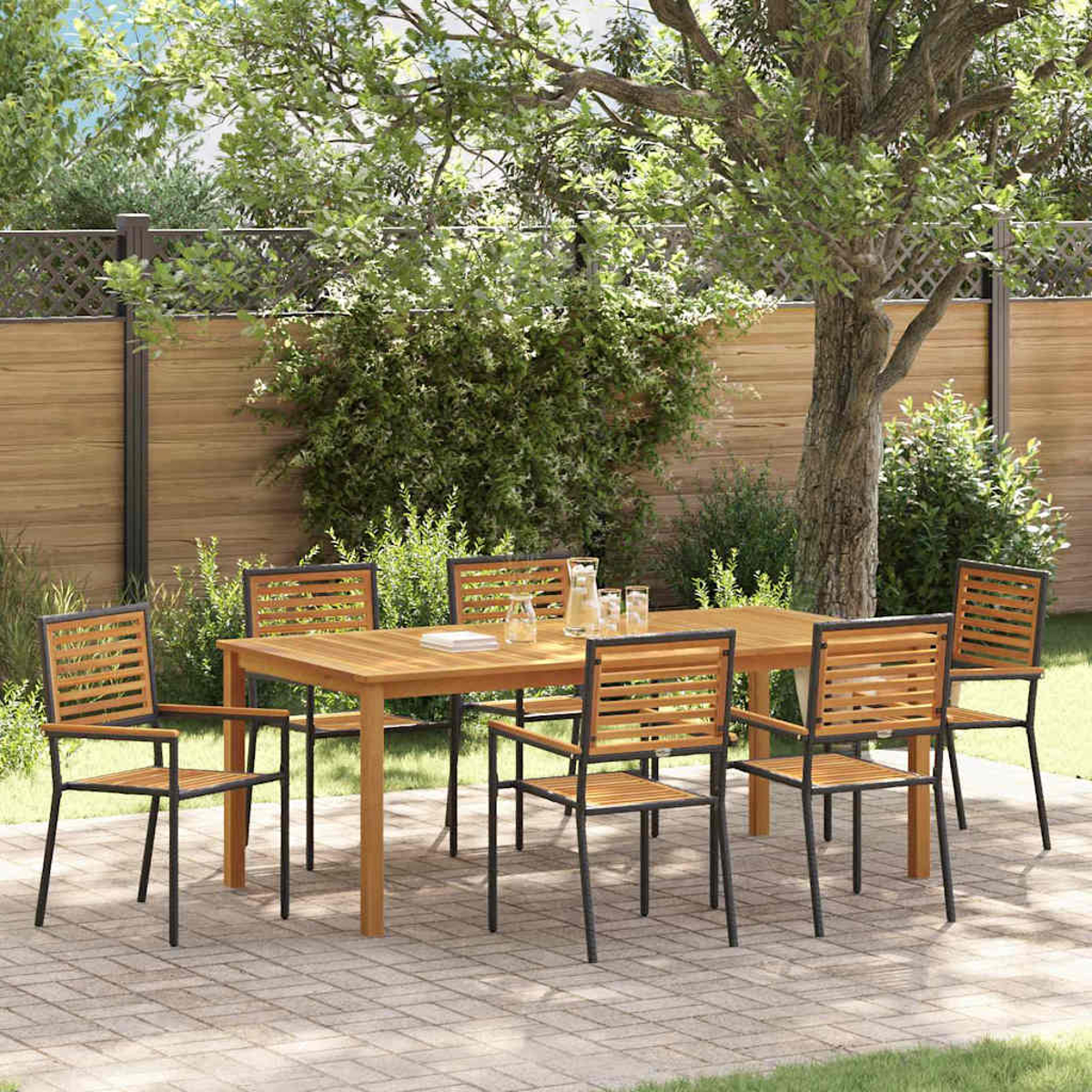 Essgarnitur im Freien: Holztisch und sechs Stühle auf einer gepflasterten Terrasse. Grüne Bäume und Sträucher im Hintergrund, mit Holzzaun.