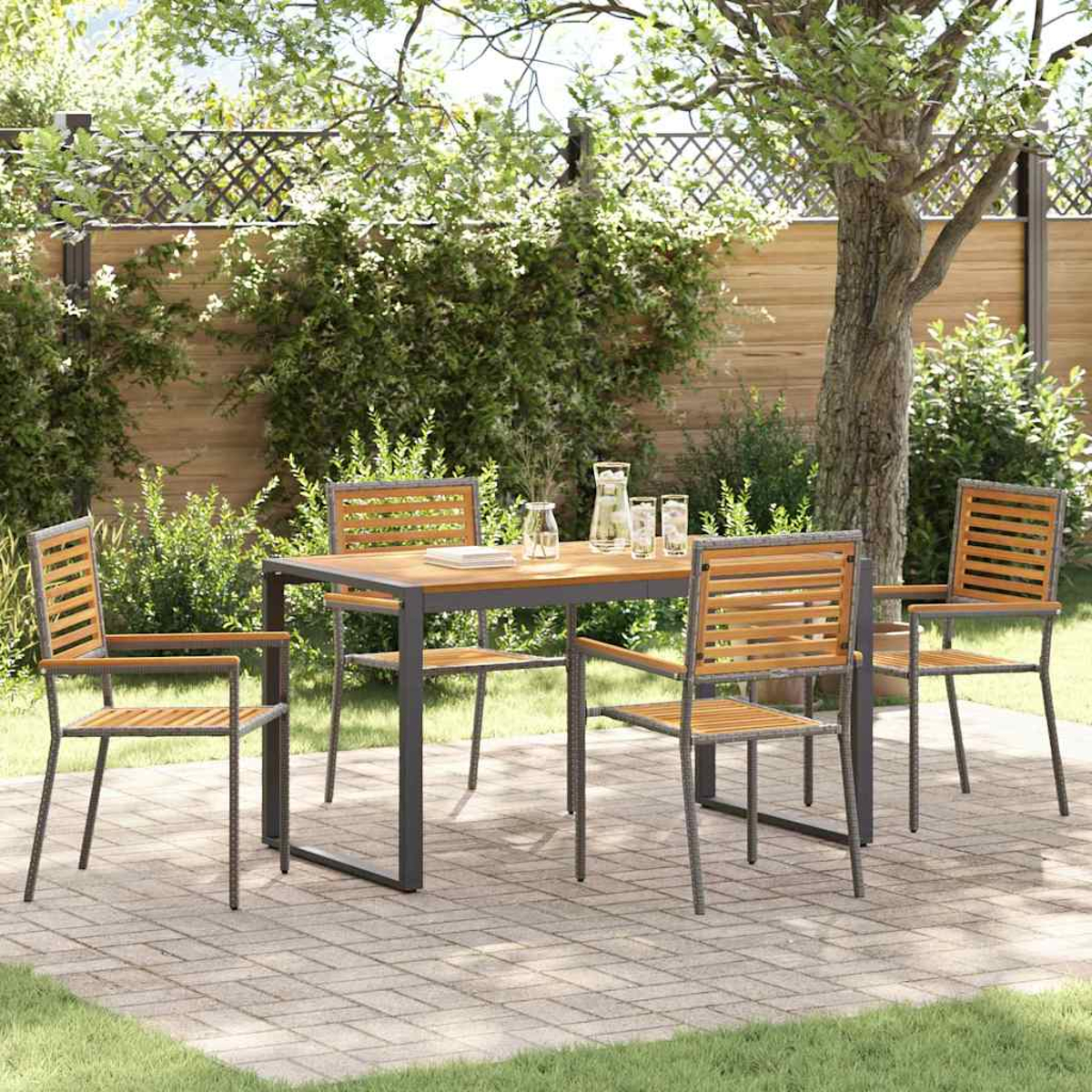 Essgarnitur im Freien mit Holztisch und Stühlen auf einer Ziegelterrasse. Grünes Gras und Bäume im Hintergrund. Krug und Gläser auf dem Tisch.