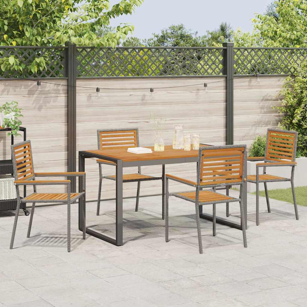 Essgruppe im Freien auf der Terrasse. Holztisch und Stühle, graue Rahmen. Hintergrund: Zaun, Grün, Lichterkette.