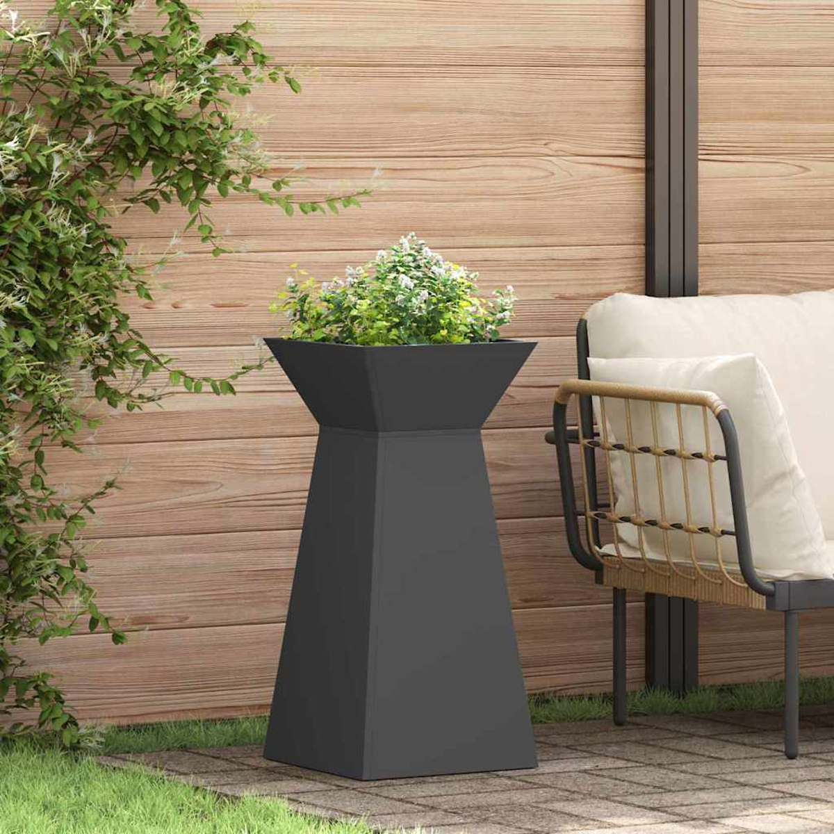 Un'alta fioriera grigio scuro con vegetazione si trova su un patio. Una recinzione di legno è dietro la fioriera, con una sedia a destra.