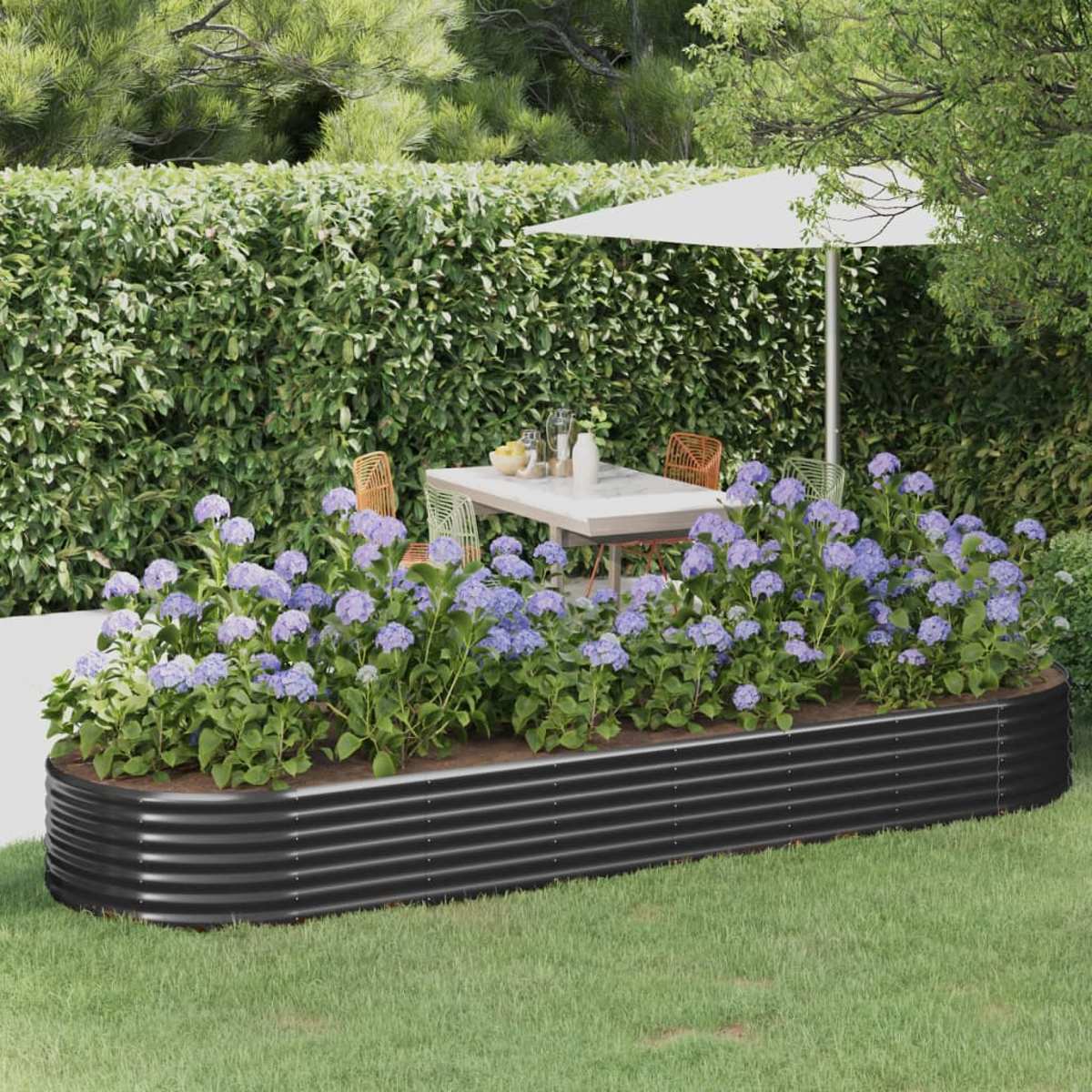 Eine Gartenszene mit einem schwarzen Hochbeet voller blauer Blumen. Im Hintergrund ein Tisch und Stühle mit einem großen Schirm.