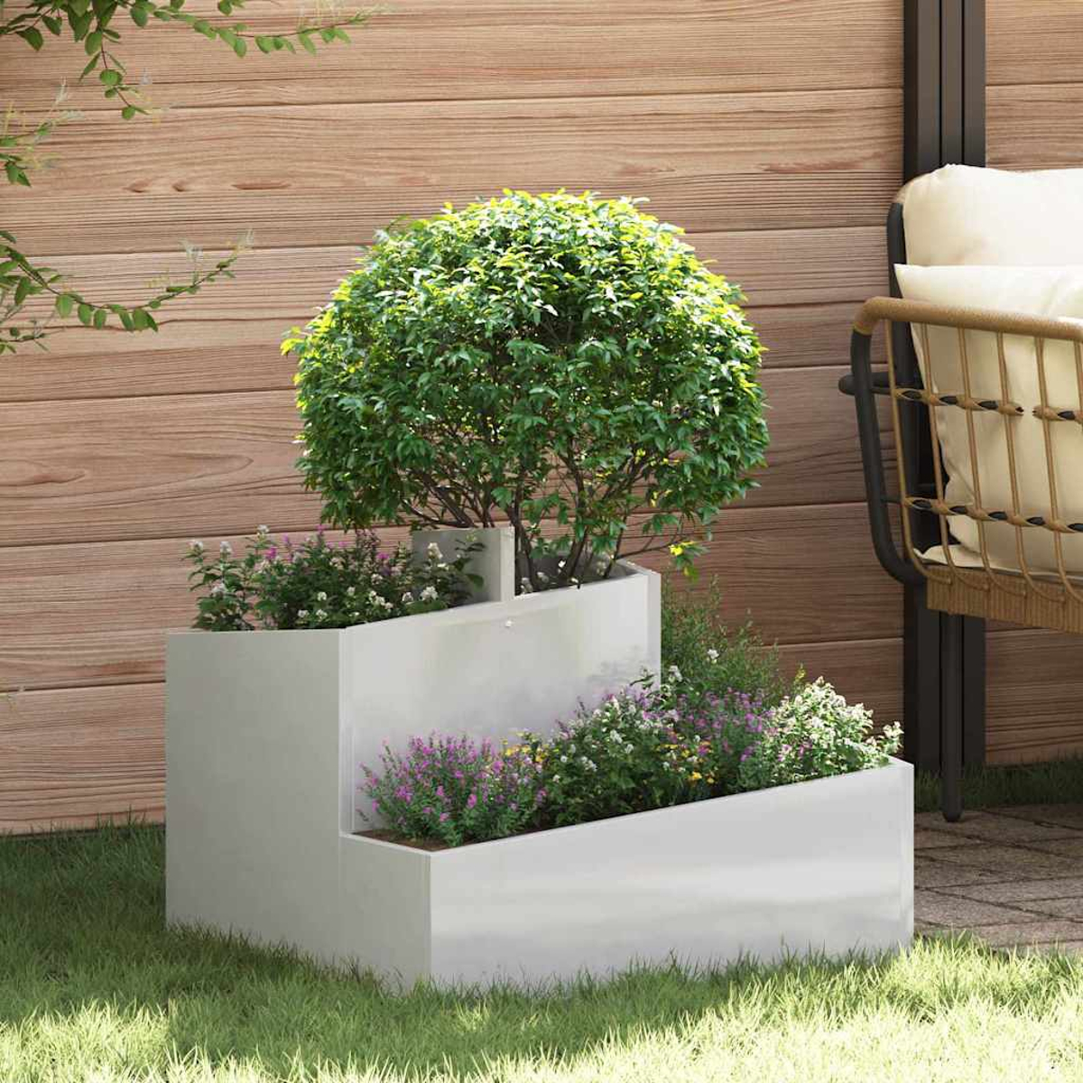 Una fioriera bianca a più livelli con piante verdi e fiori è sull'erba. Una recinzione in legno e una sedia sullo sfondo.
