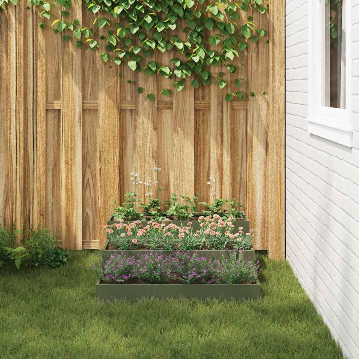 Un'aiuola a gradoni con fiori rosa e viola sull'erba. Una recinzione di legno sullo sfondo, con un muro di mattoni bianchi a destra.