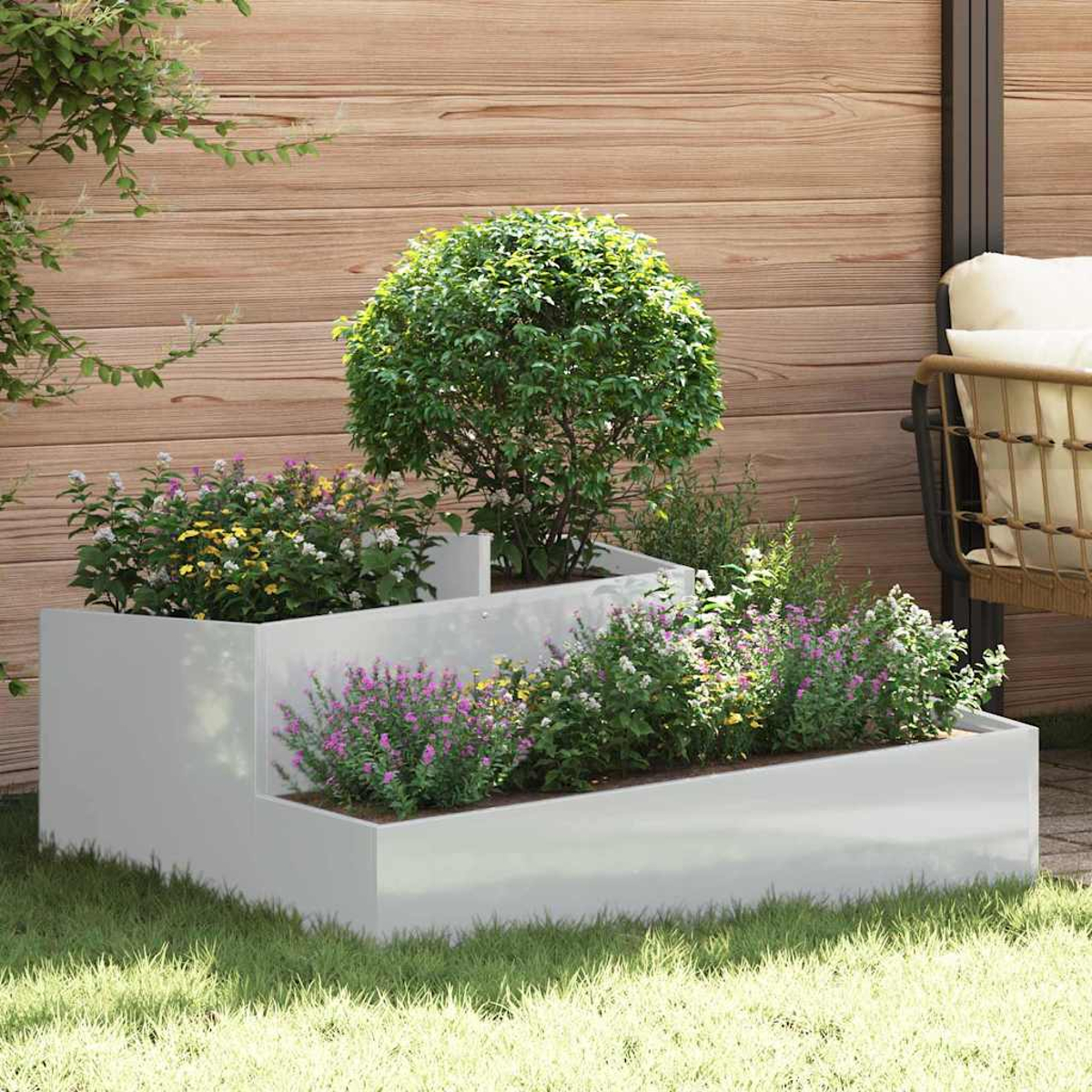 Una fioriera bianca a gradoni con fiori e un alberello. Una staccionata di legno e una sedia sullo sfondo, tutto sull'erba.