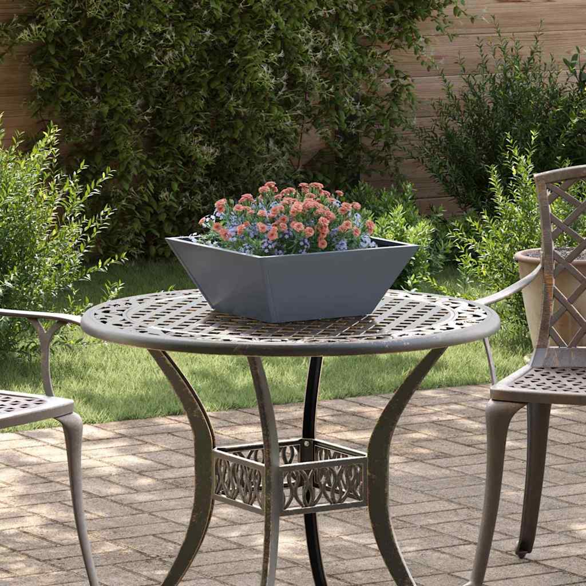 Una scena del patio. Un tavolo di metallo con un vaso di fiori pieno di fiori rosa e blu. Una sedia di metallo e una vegetazione lussureggiante.