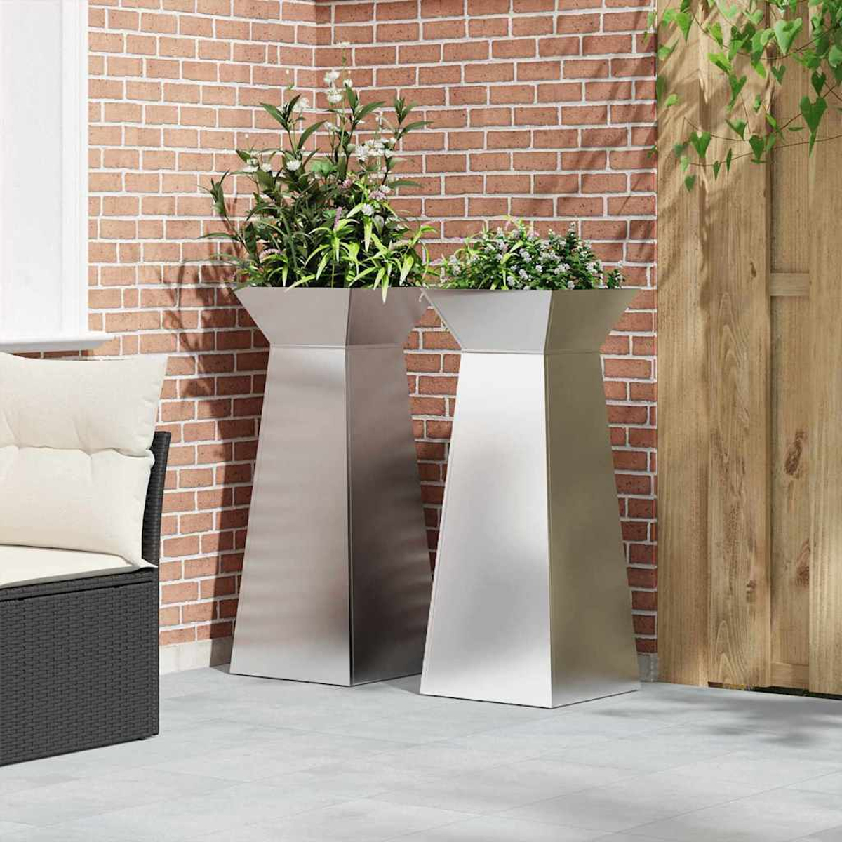 Due fioriere in metallo con piante su un patio. Muro di mattoni rossi e staccionata di legno sullo sfondo. Una sedia a sinistra.