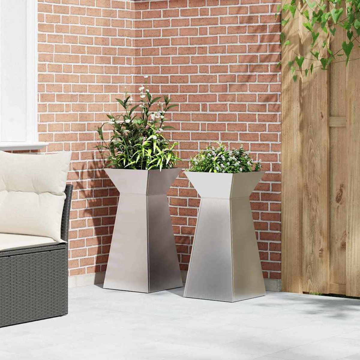 Due fioriere metalliche con piante su un patio. Un muro di mattoni e una recinzione di legno sullo sfondo. Una sedia a sinistra.