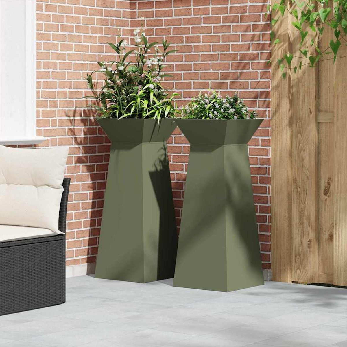 Due fioriere verde oliva con piante su un patio. Muro di mattoni rossi dietro. Recinzione di legno a destra. Sedia nera a sinistra.