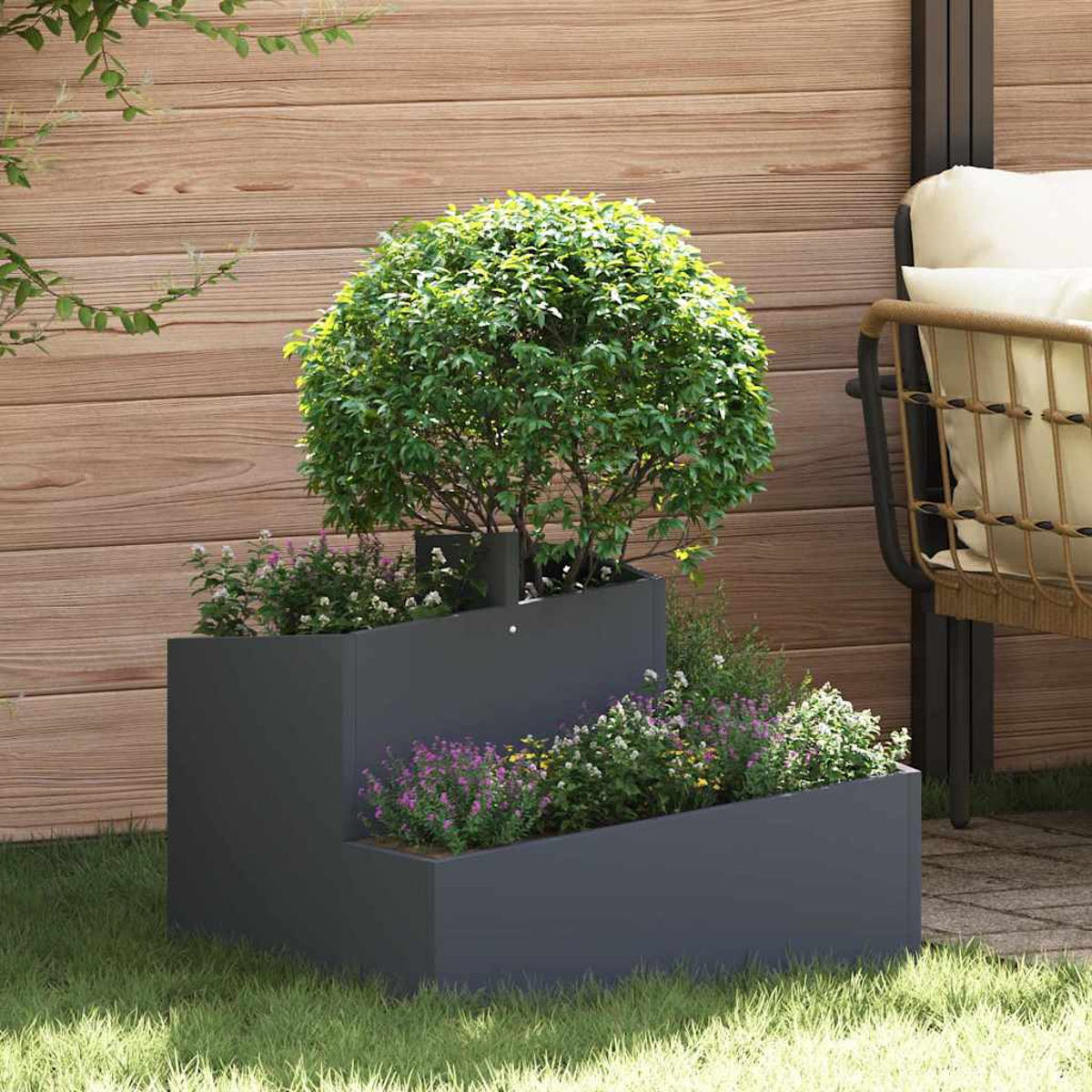 Una fioriera grigio scuro a più livelli con un cespuglio verde e fiori colorati. Una recinzione di legno e una sedia sono sullo sfondo.