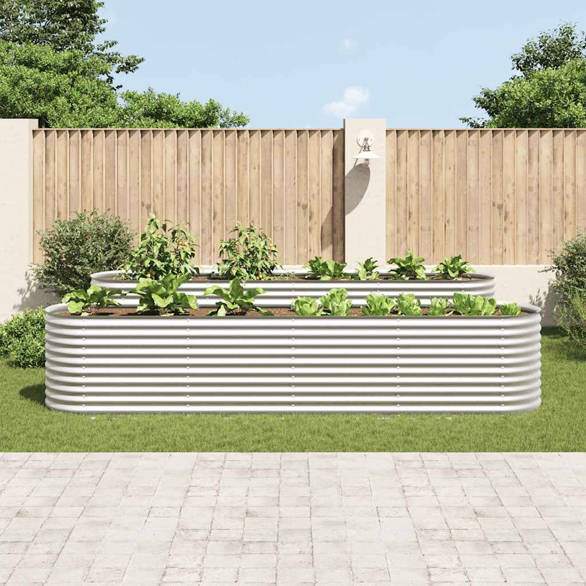 Zwei erhöhte Metall-Gartenbeete mit Pflanzen. Ein Holzzaun und beiger Pfeiler im Hintergrund. Grünes Gras und ein gepflasterter Gehweg davor.