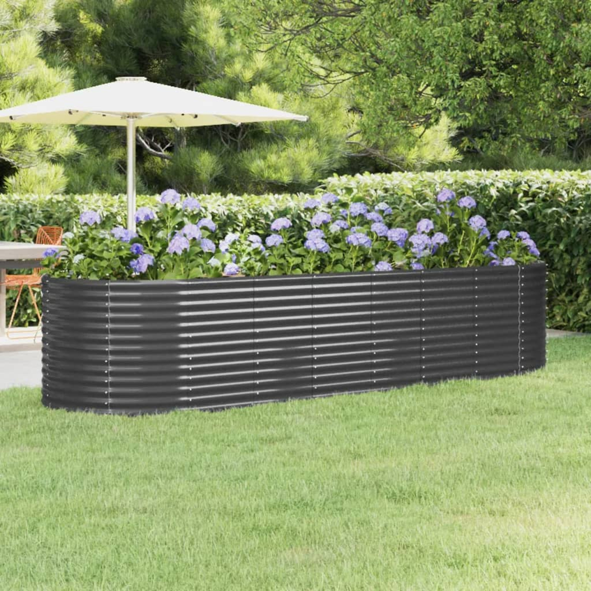 Ein graues, erhöhtes Gartenbeet aus Metall mit lila Blumen, auf grünem Gras, mit einem weißen Schirm und Bäumen im Hintergrund.
