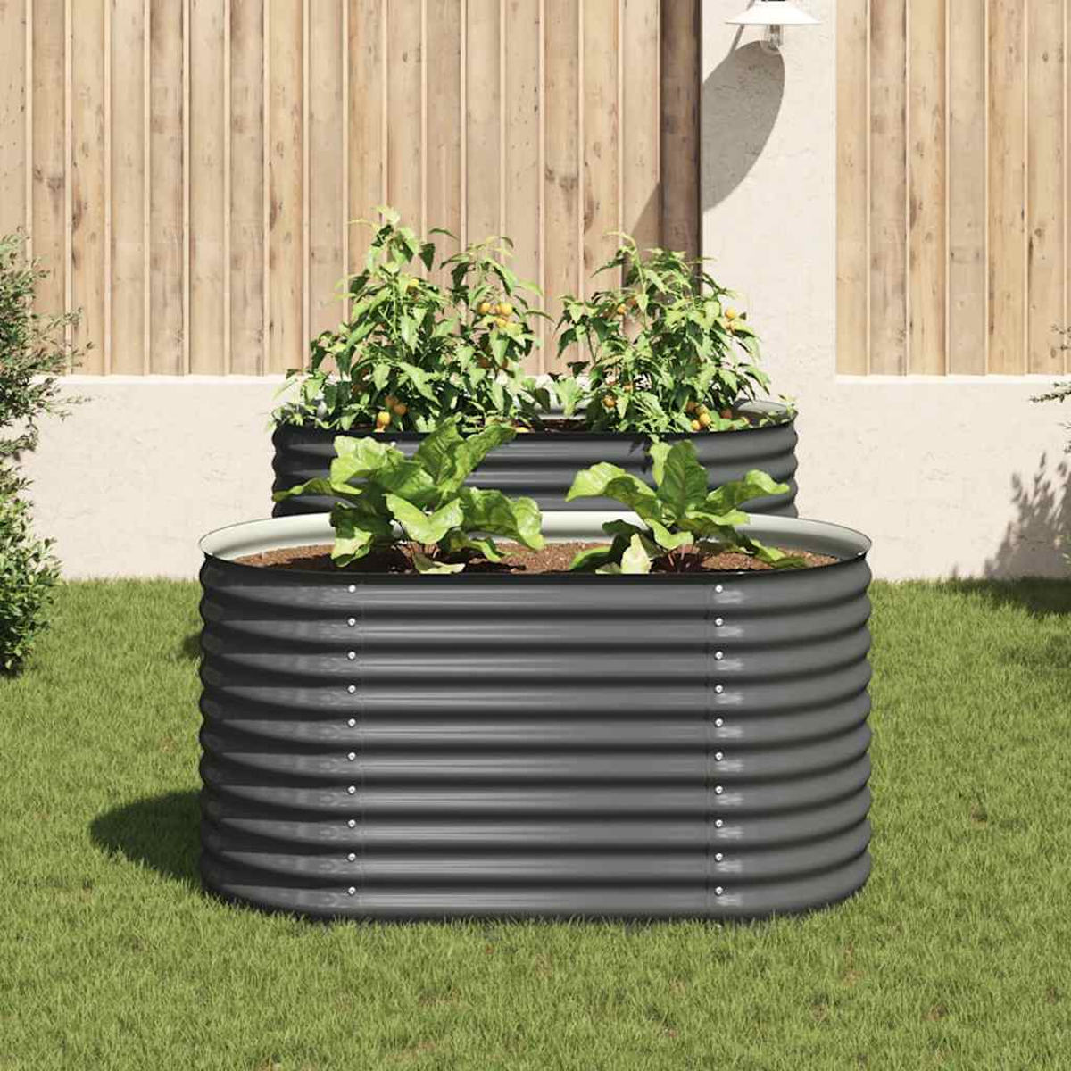 Zwei Metall-Gartenbeete mit Pflanzen stehen auf Gras. Im Hintergrund ist ein Holzzaun. Ein Beet steht vor dem anderen.