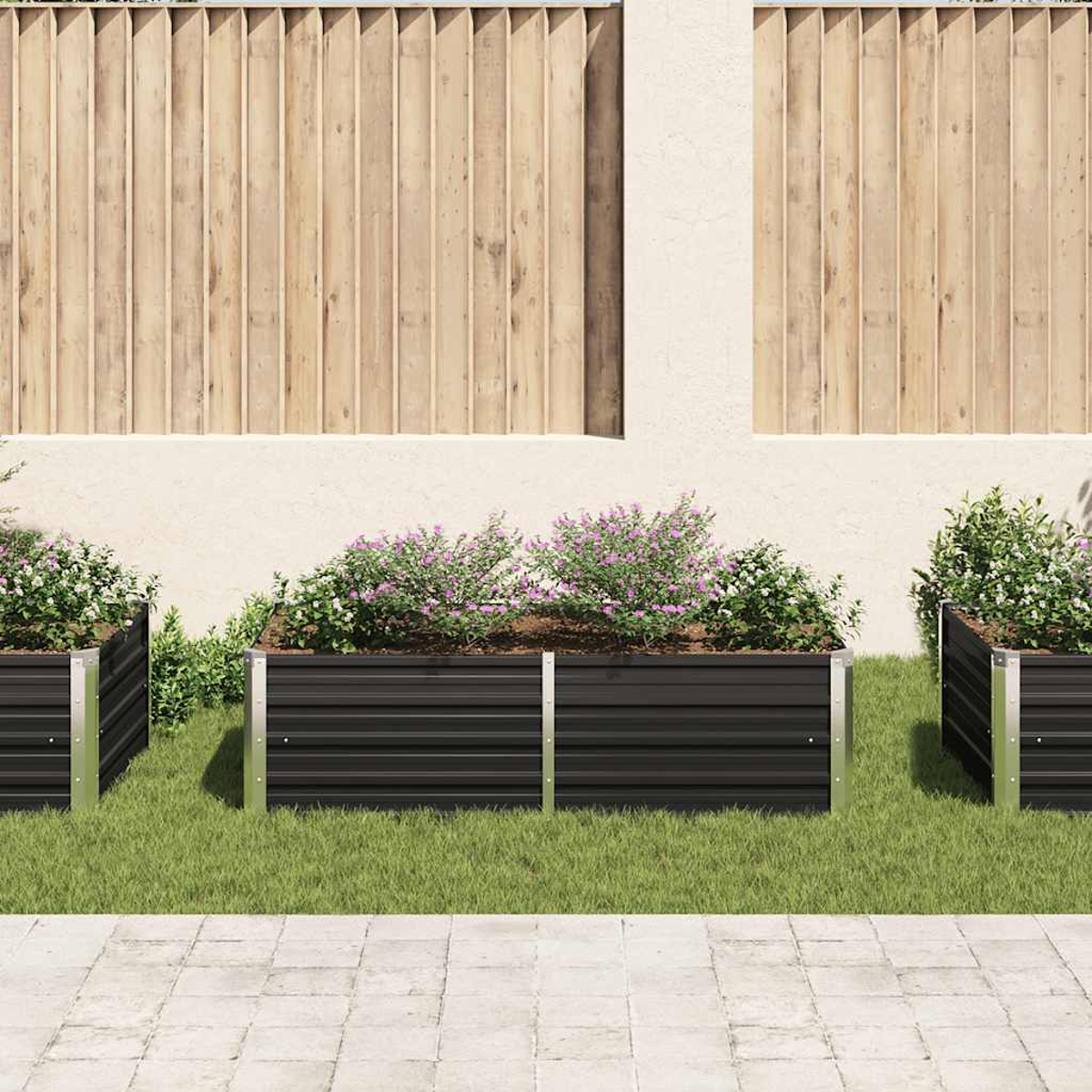 Drei schwarze Metallpflanzkästen mit Blumen auf grünem Gras. Im Hintergrund ist ein Holzzaun. Pflasterung im Vordergrund.