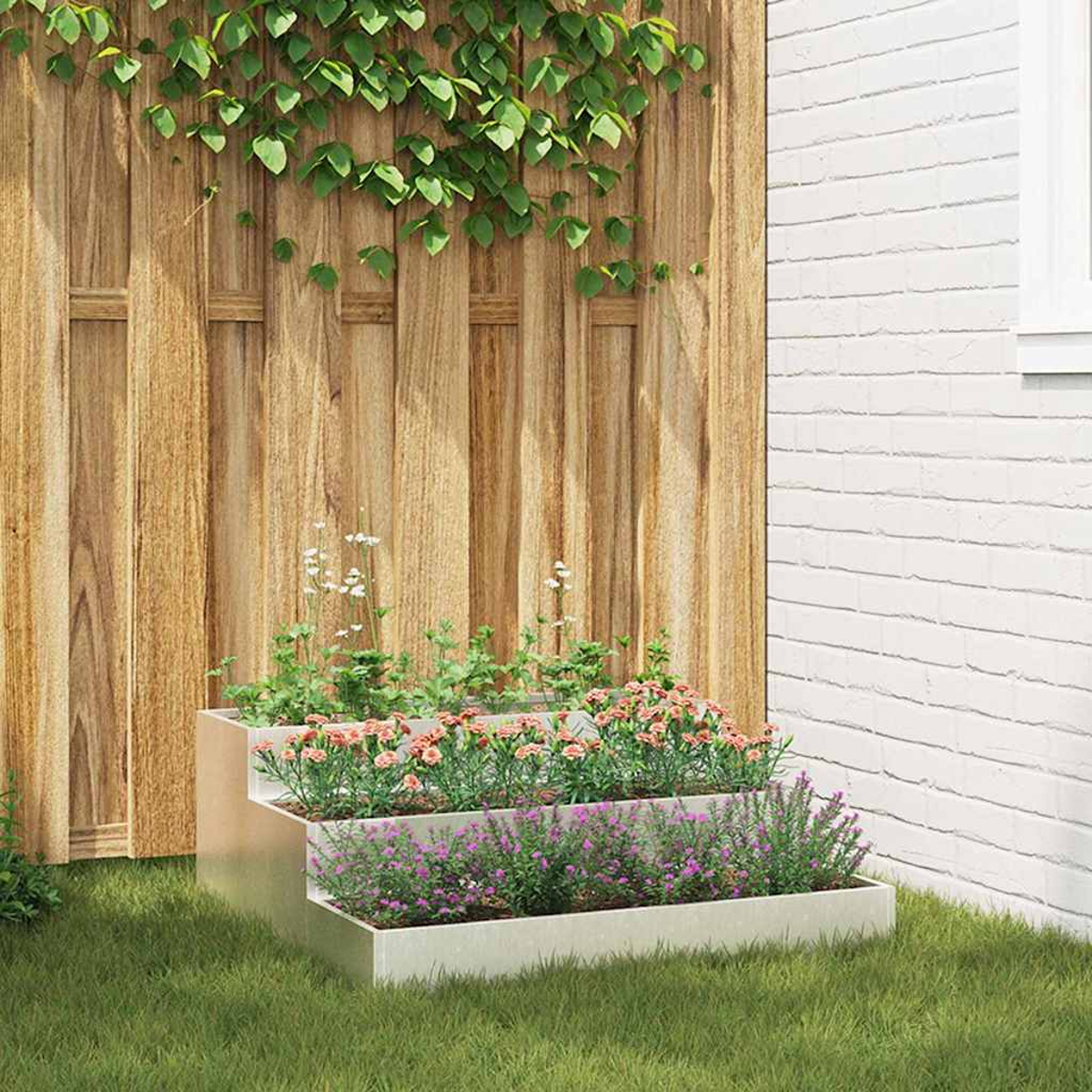 Una fioriera a gradini piena di fiori rosa e viola si trova sull'erba. Sullo sfondo una staccionata in legno e un muro di mattoni bianchi.