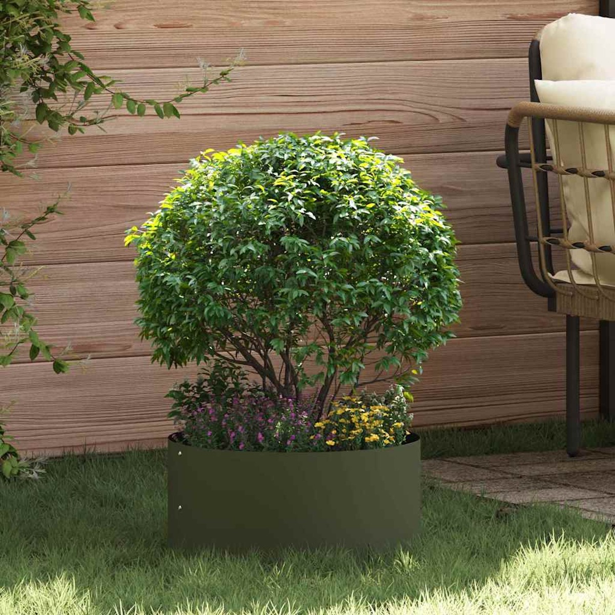 Un cespuglio verde in una fioriera verde scuro con fiori viola e gialli, su erba, con uno sfondo di recinzione in legno e una sedia.