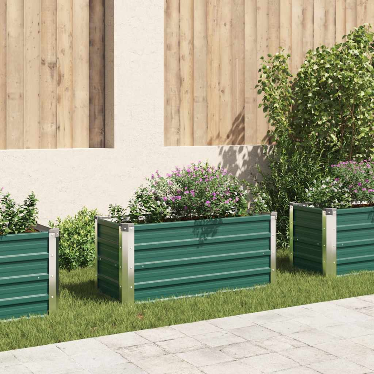 Drei grüne Metallpflanzkästen mit Blumen auf einem Rasen, im Hintergrund ein Holzzaun und eine beige Wand.