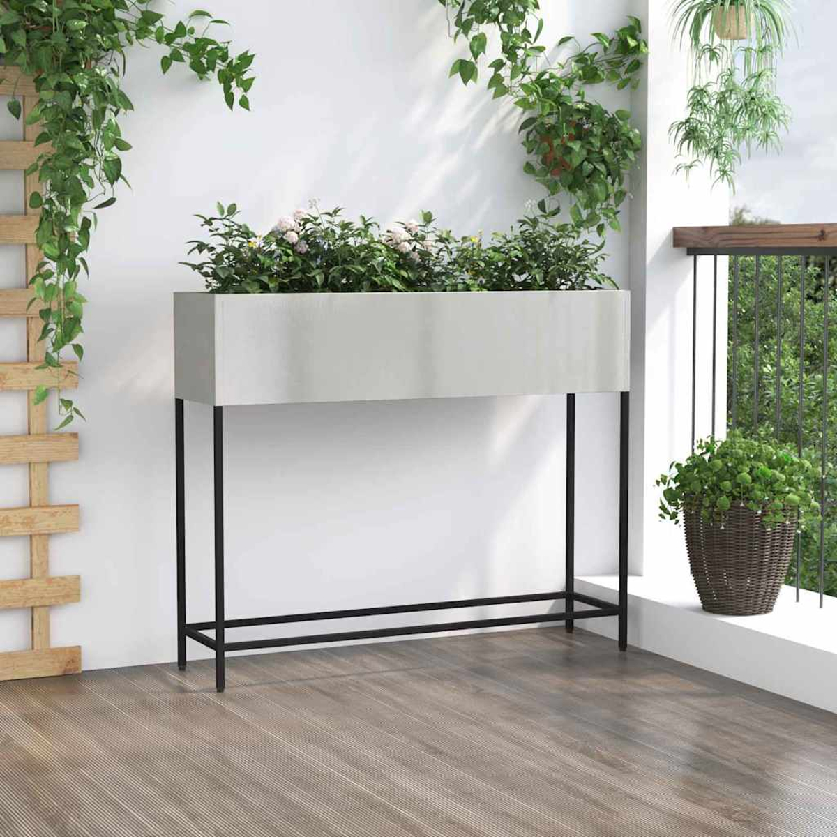 Una fioriera rettangolare grigia con fiori poggia su gambe in metallo nero. Viti e piante verdi la circondano, con un pavimento in legno davanti.