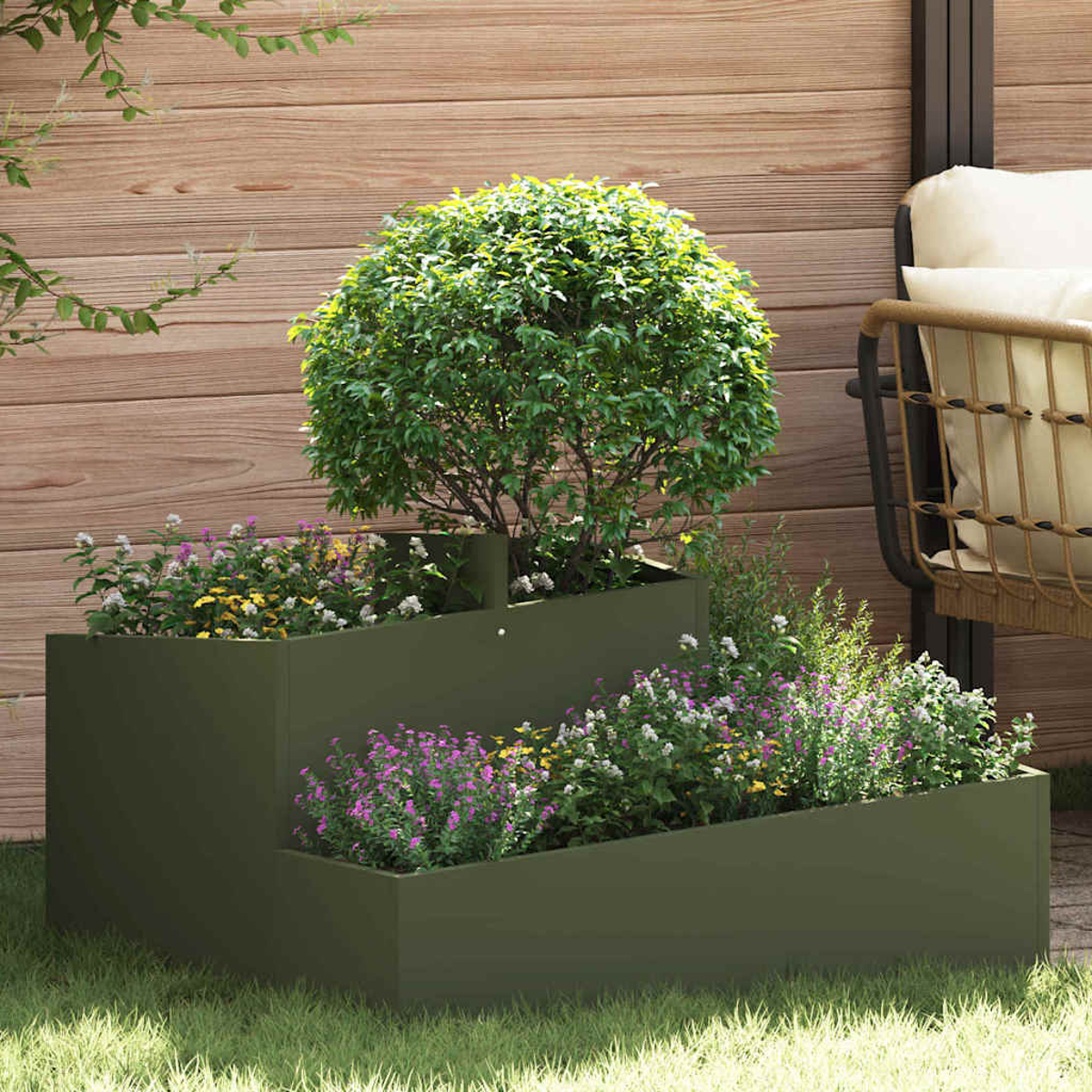 Una fioriera verde a più livelli con fiori e un albero si trova sull'erba. Una recinzione di legno e una sedia sullo sfondo.