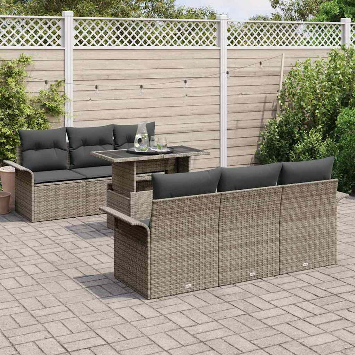 Terrassenmöbel mit grauen Kissen und einem Tisch. Vor Holzzaun mit Grün. Gepflasterte Steinterrasse.
