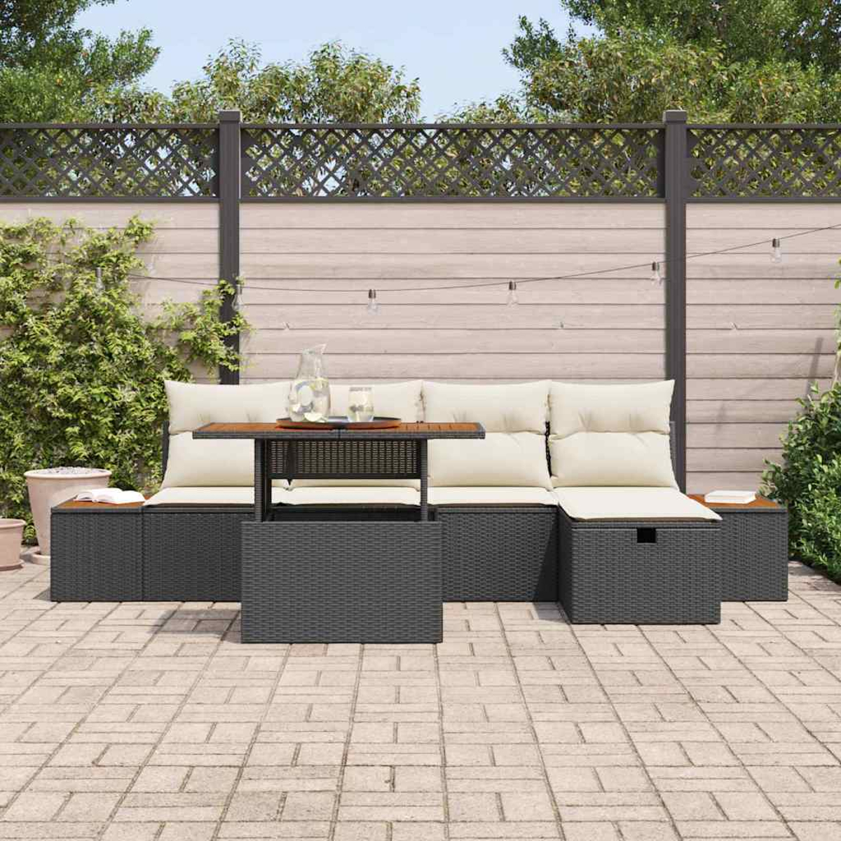Terrassenset im Freien mit grauem Korbboden, Holztisch und cremefarbenen Kissen. Auf dem Tisch stehen eine Wasserkaraffe und Gläser, im Hintergrund ein Zaun.