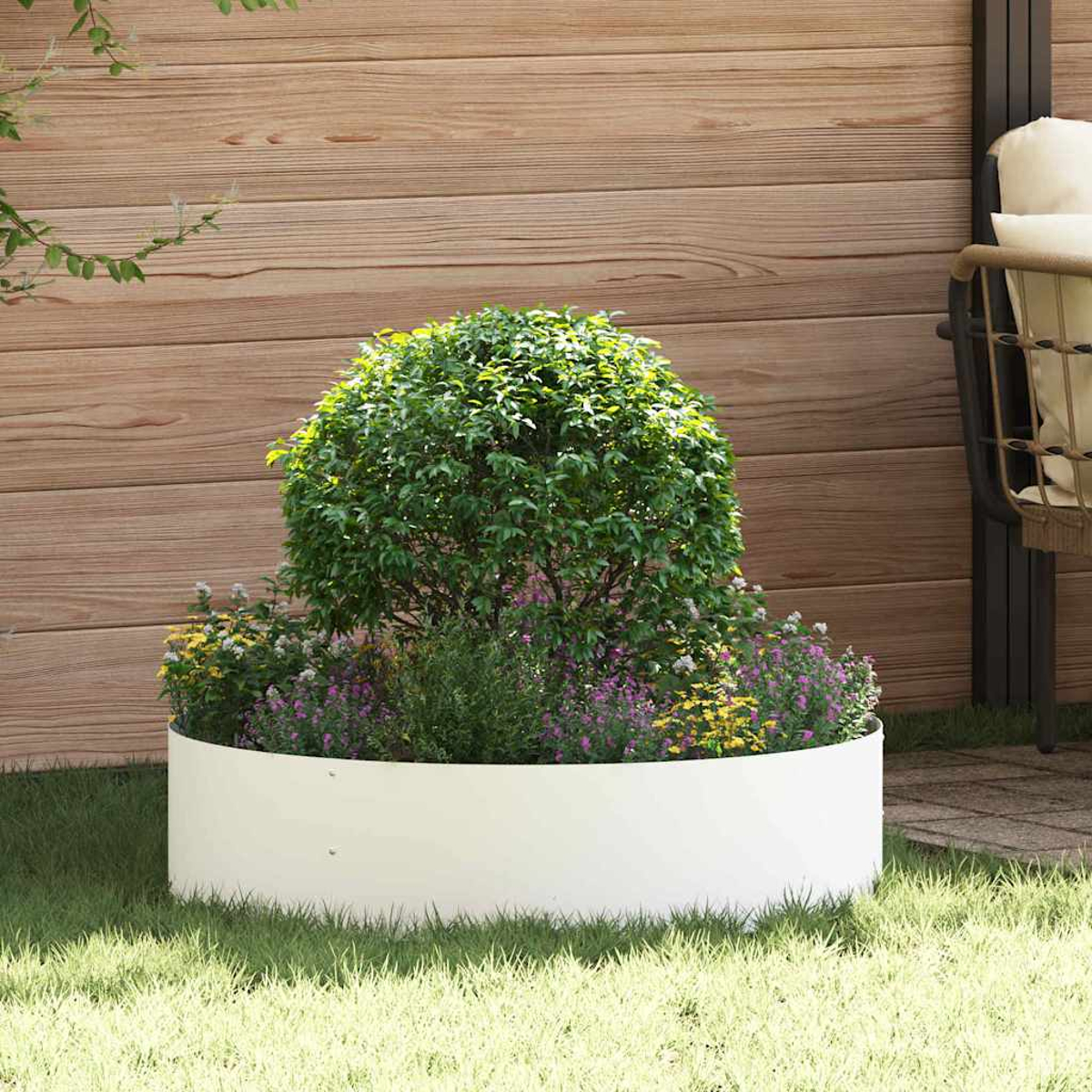 Una fioriera bianca circolare contiene un cespuglio verde e fiori colorati. Una recinzione di legno è sullo sfondo, con erba in primo piano.